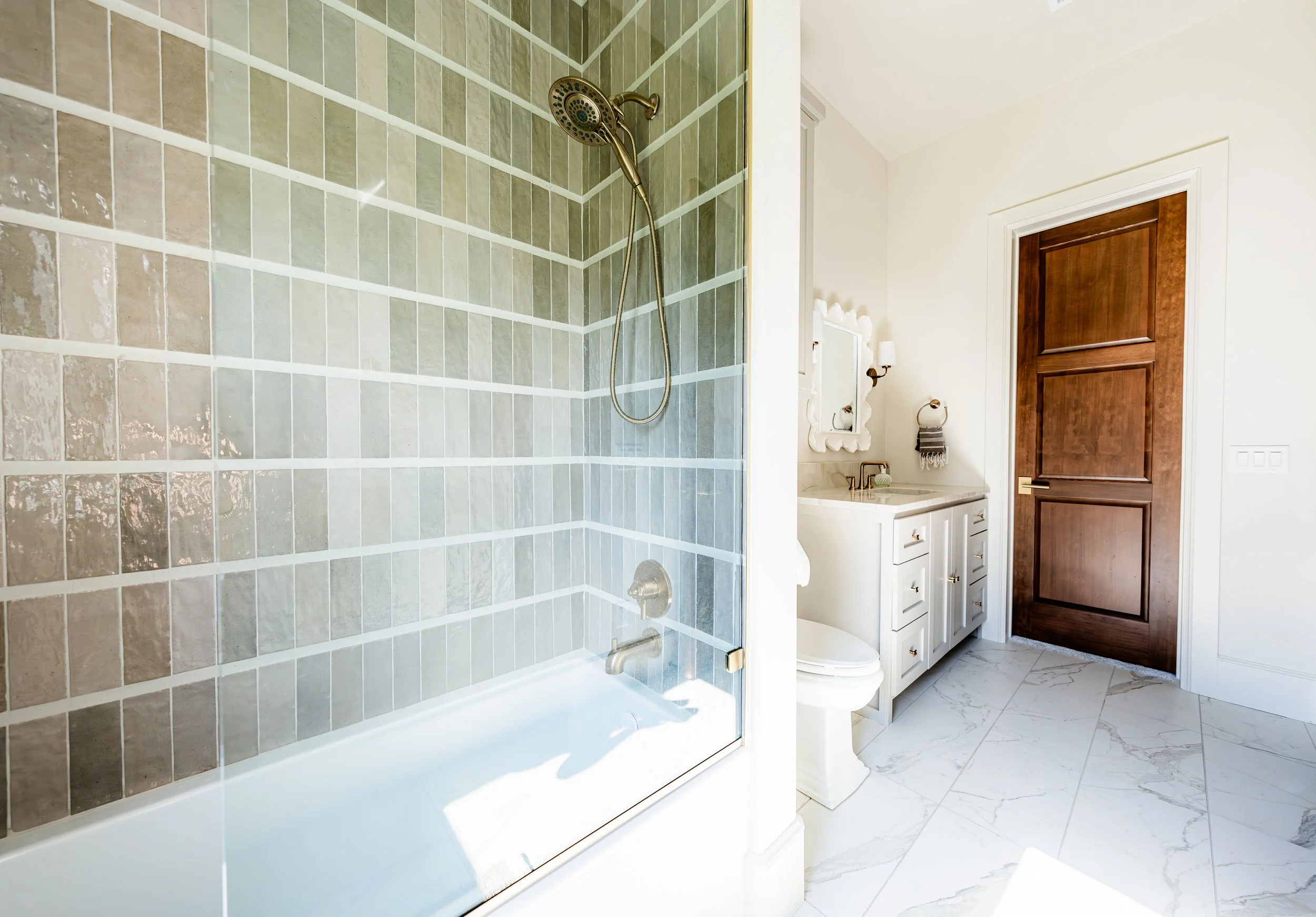 Bathroom with a tiled shower, white vanity with sink, mirror, towel, toilet, and wooden door.