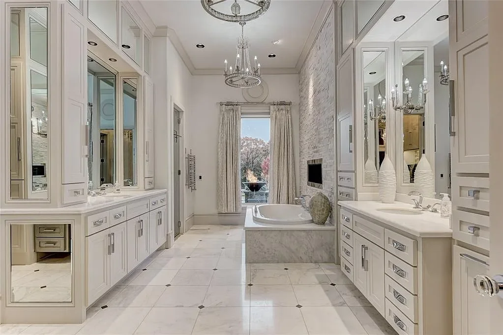 Luxury bathroom with white cabinetry, a bathtub, double sinks, marble flooring, and chandeliers.