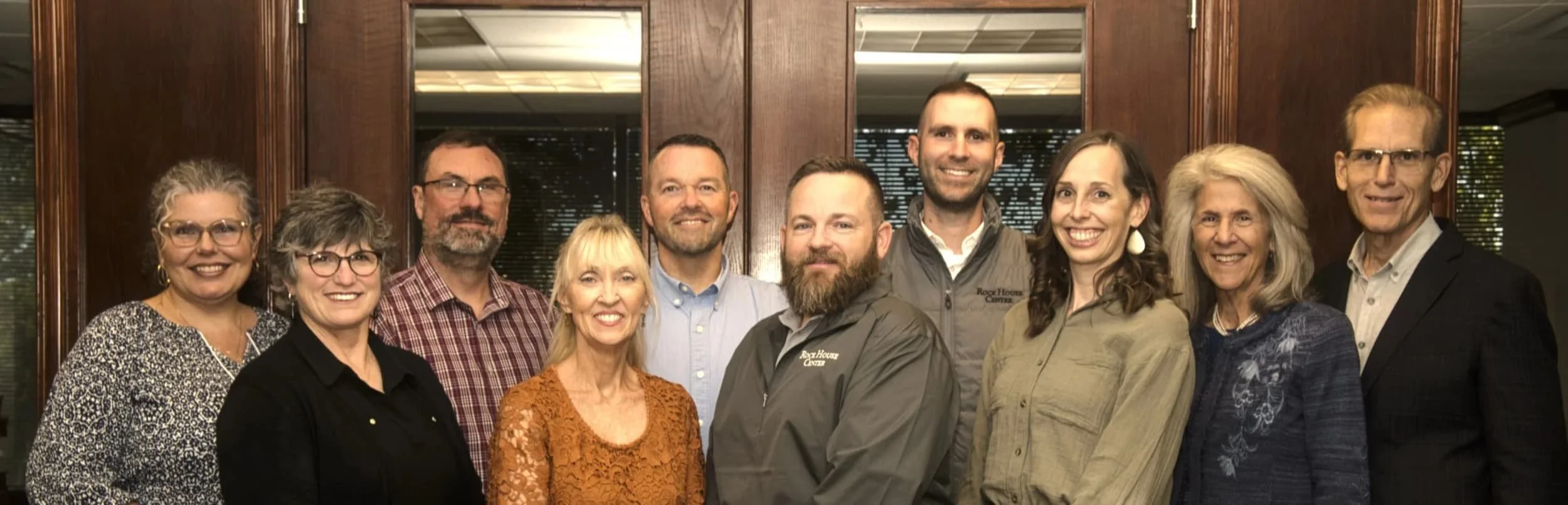 Rock House Center Team.  Wendy, Patti, Steve, Holly, John, Joe, Nathan, Michelle, Beth and John Murphy. (Left to right) in front of a dark conference room door.