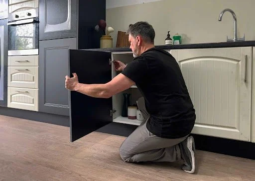Homeowner installing or adjusting a kitchen cabinet door during a kitchen remodeling project, demonstrating a non-structural home improvement that typically does not require a building permit in Raleigh.