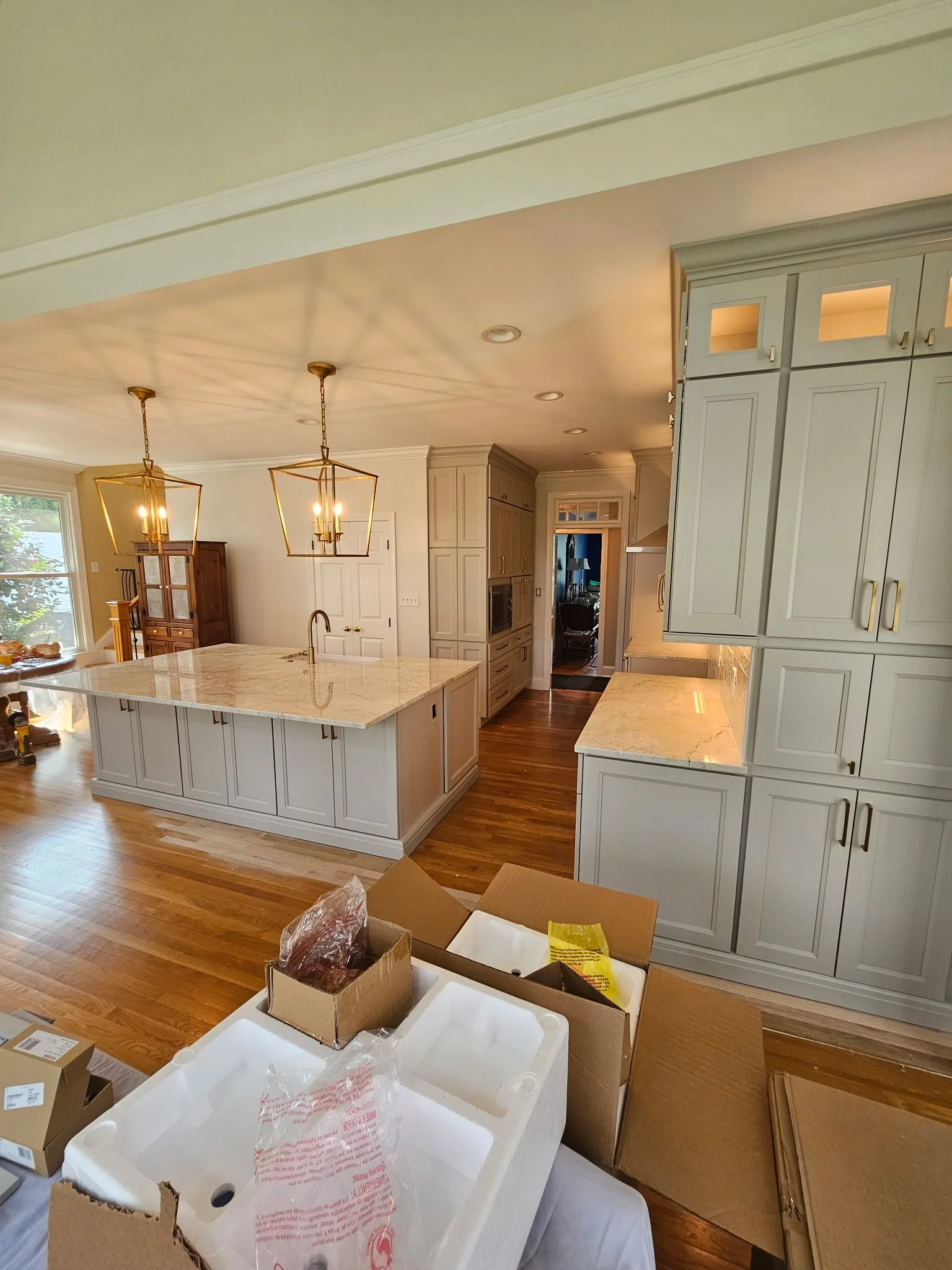 A spacious kitchen with light-colored cabinetry, an island with a marble countertop, hardwood floors, and modern hanging light fixtures.
