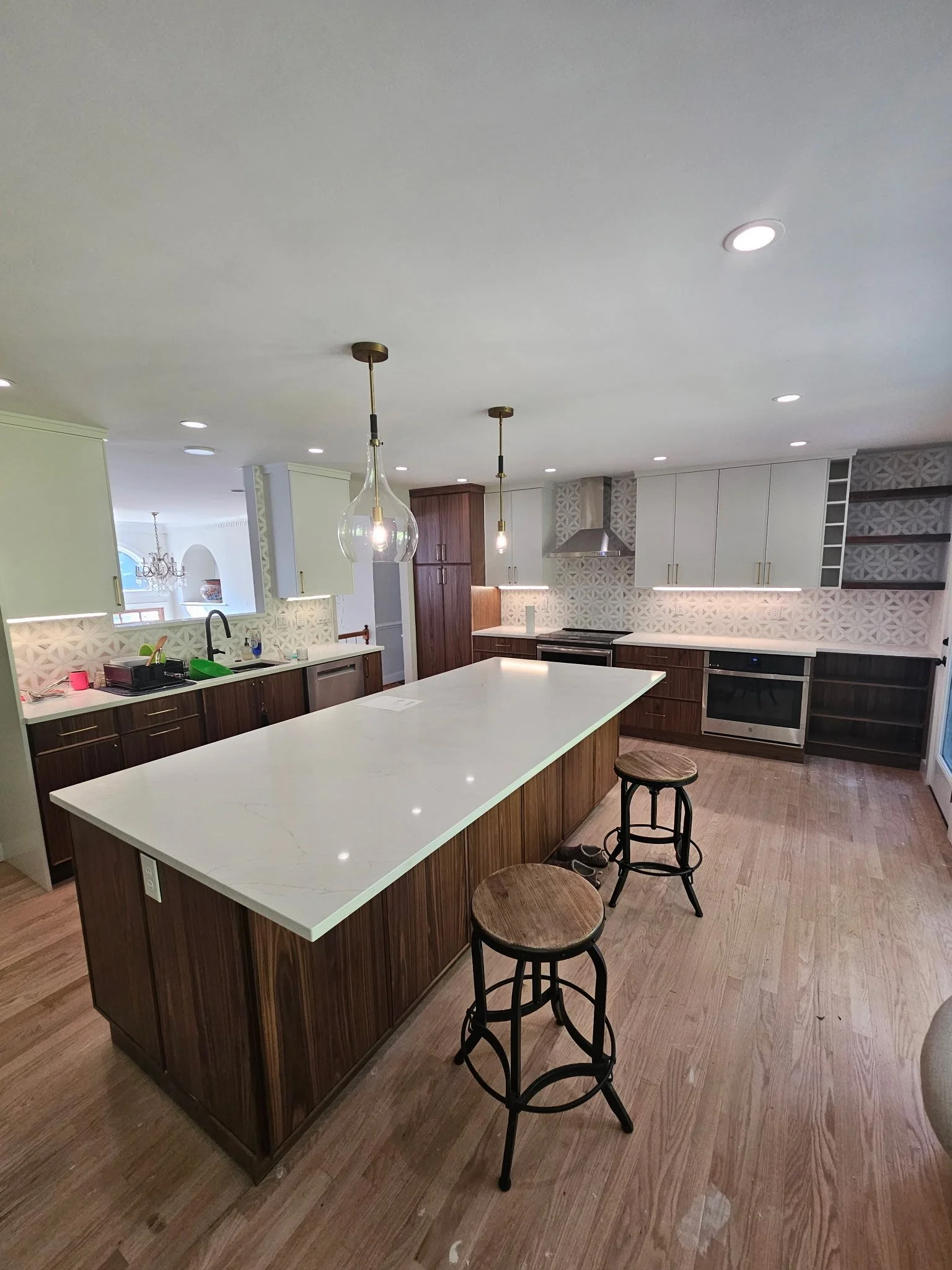 Modern kitchen with white countertops, dark wood cabinets, and a large central island with two stools, pendant lights, and built-in appliances.