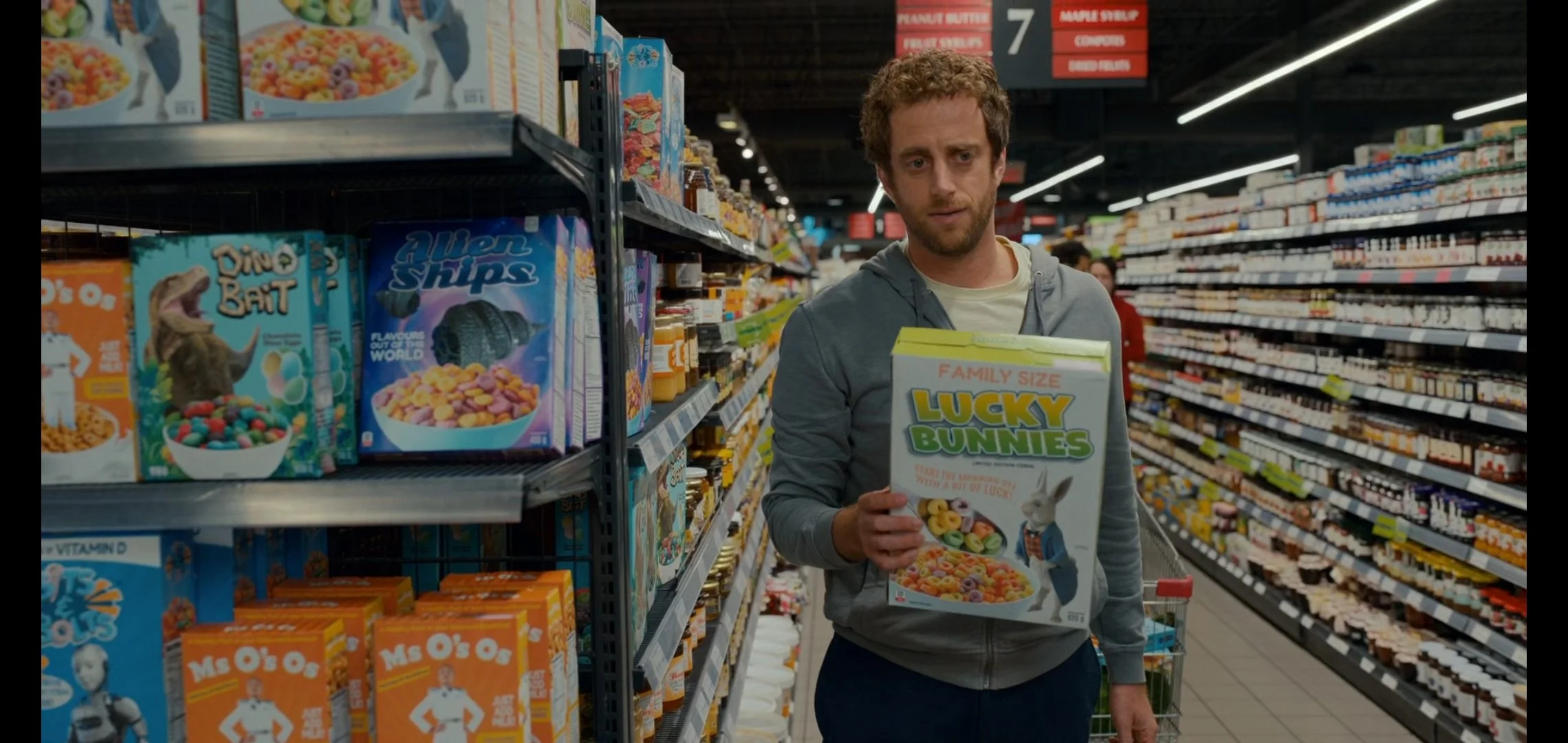 A man holding a box of Lucky Bunnies cereal while shopping in a grocery store aisle with colorful cereal boxes on shelves.