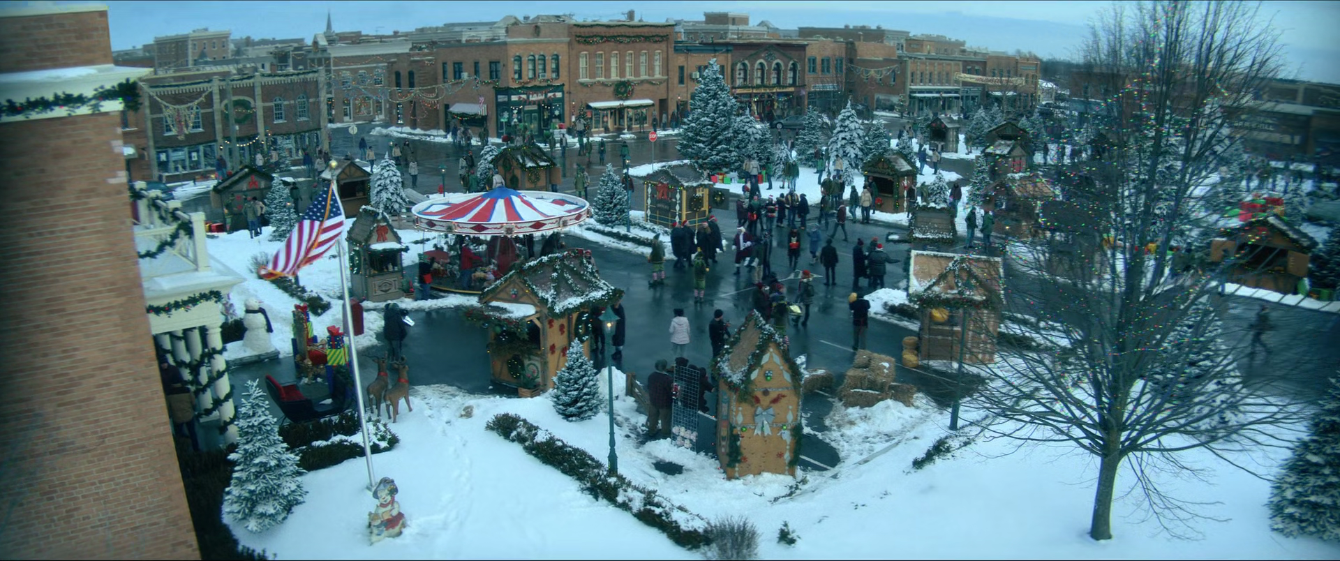 A snow-covered town square decorated for Christmas with festive lights, ornaments, and holiday-themed booths. People are walking around, some in Santa hats, enjoying the holiday atmosphere. Christmas trees and small wooden stalls are scattered throughout the area.