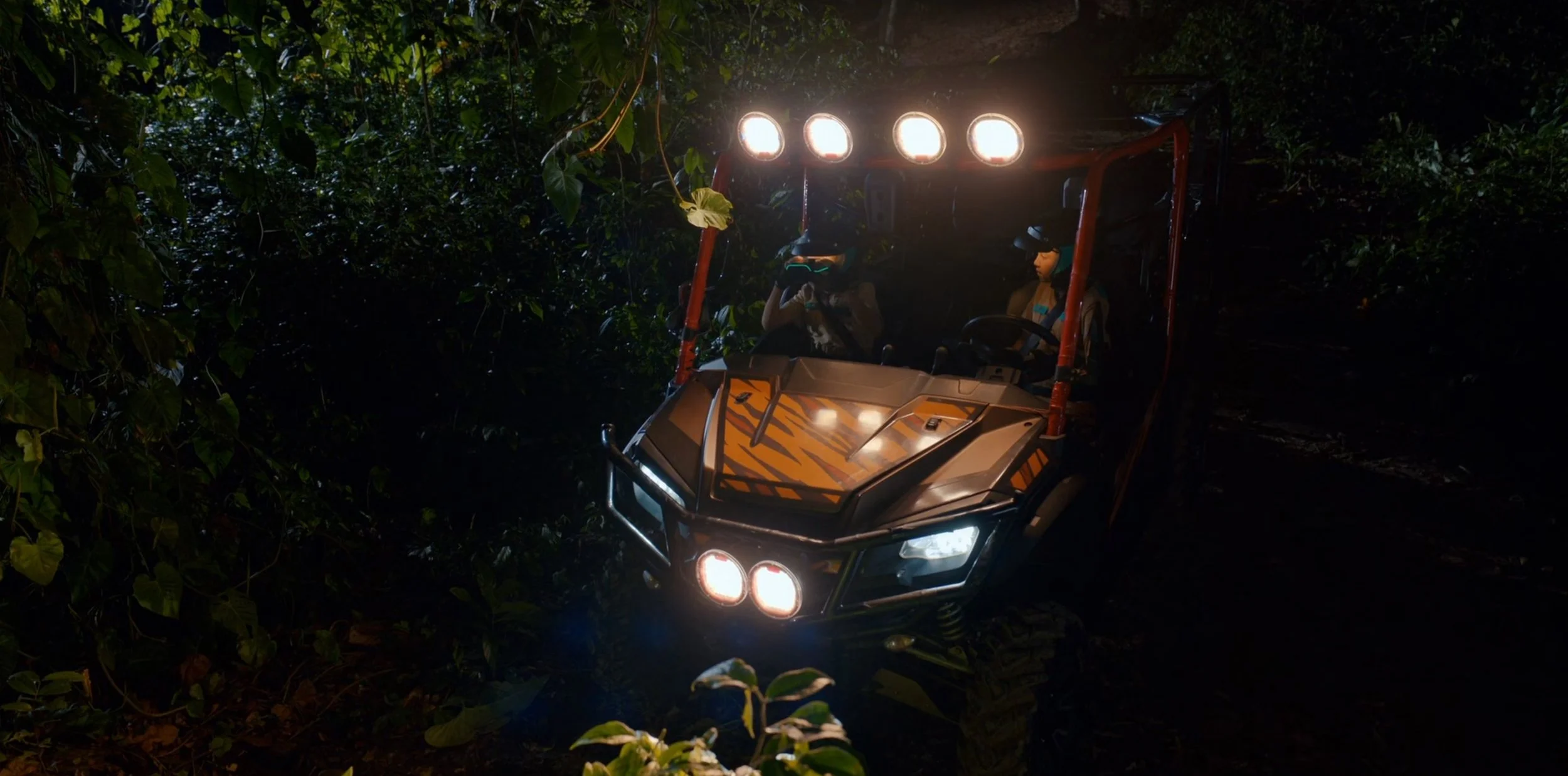 A utility terrain vehicle (UTV) with bright headlights driving through a dark forest.