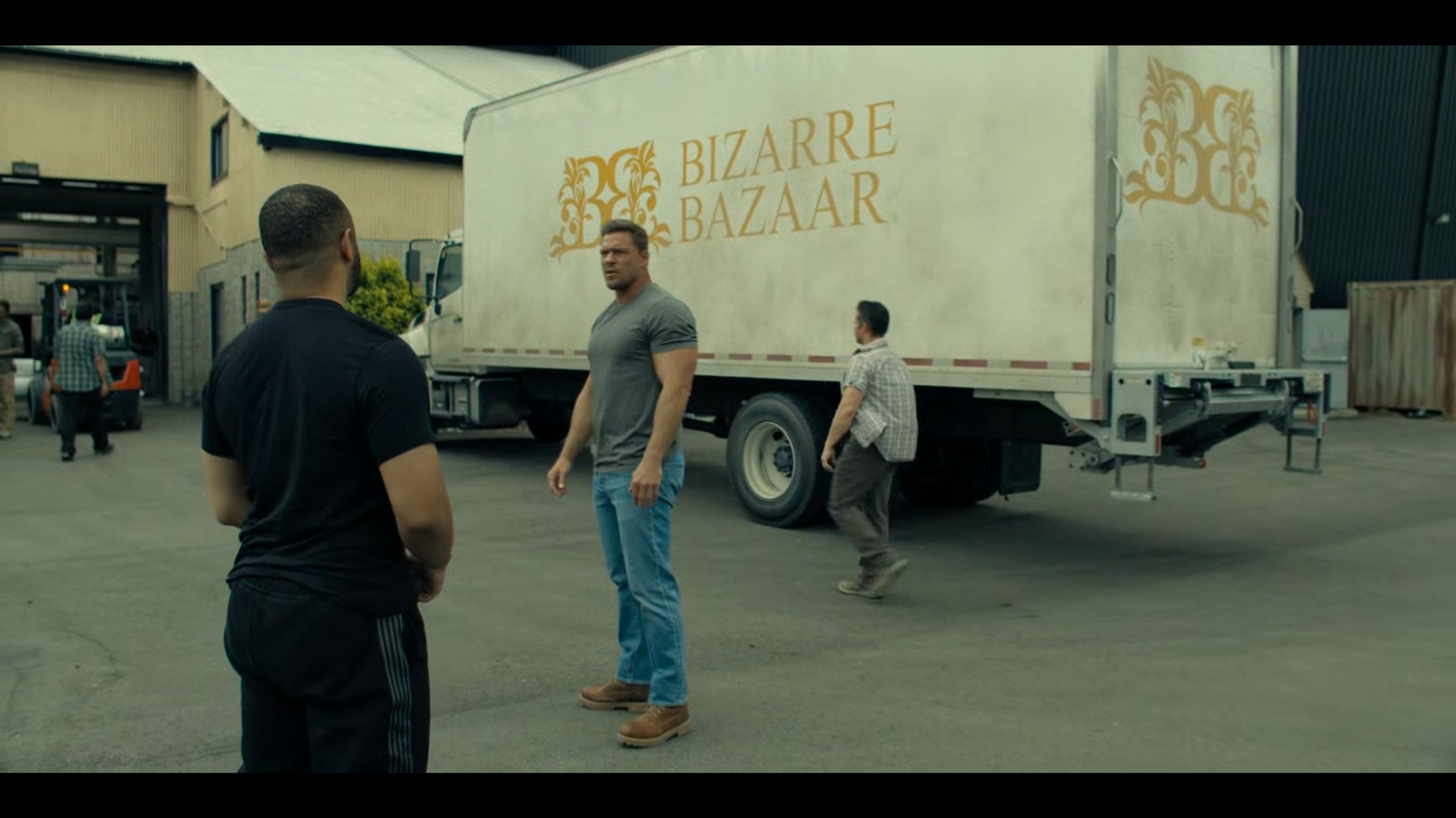 People standing in front of a truck with the words 'Bizarre Bazaar' on the side in a parking lot or back alley.