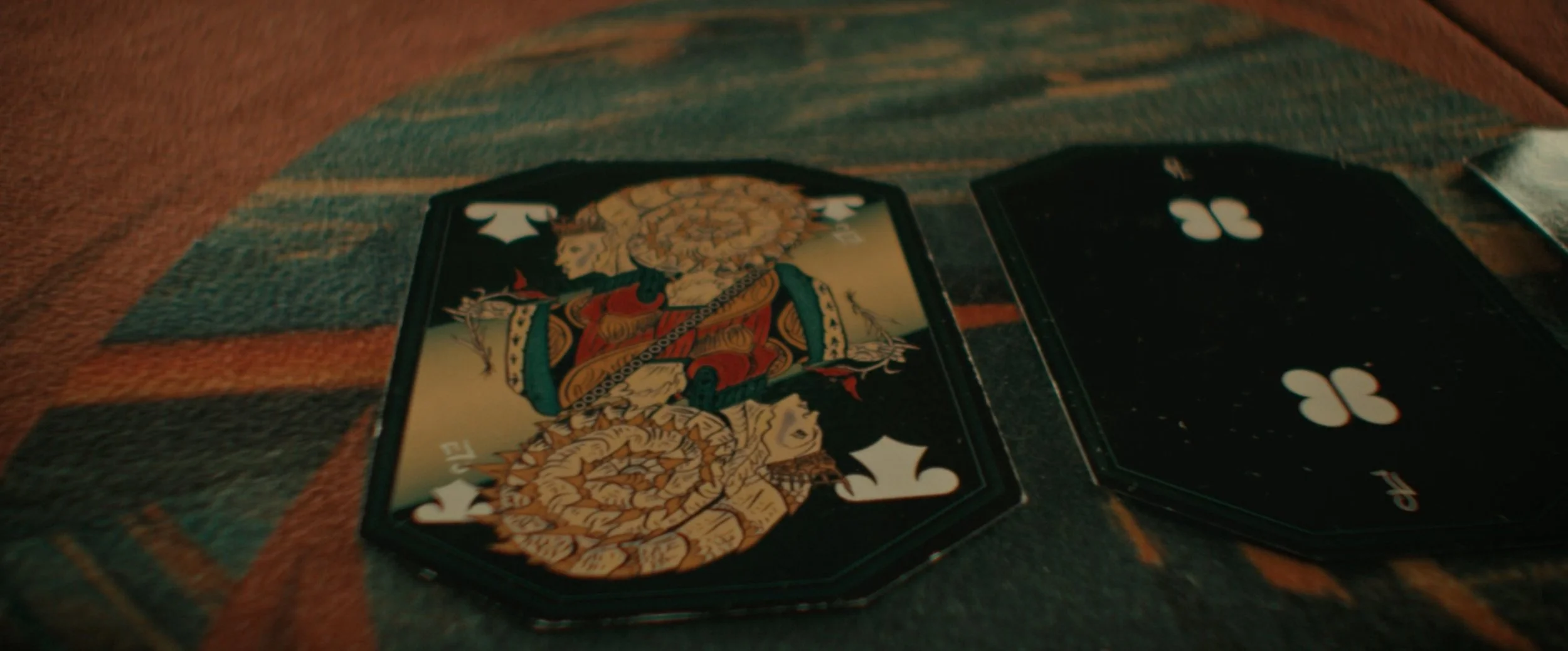 A close-up of playing cards on a cat-themed scratched poker chip and striped fabric surface.