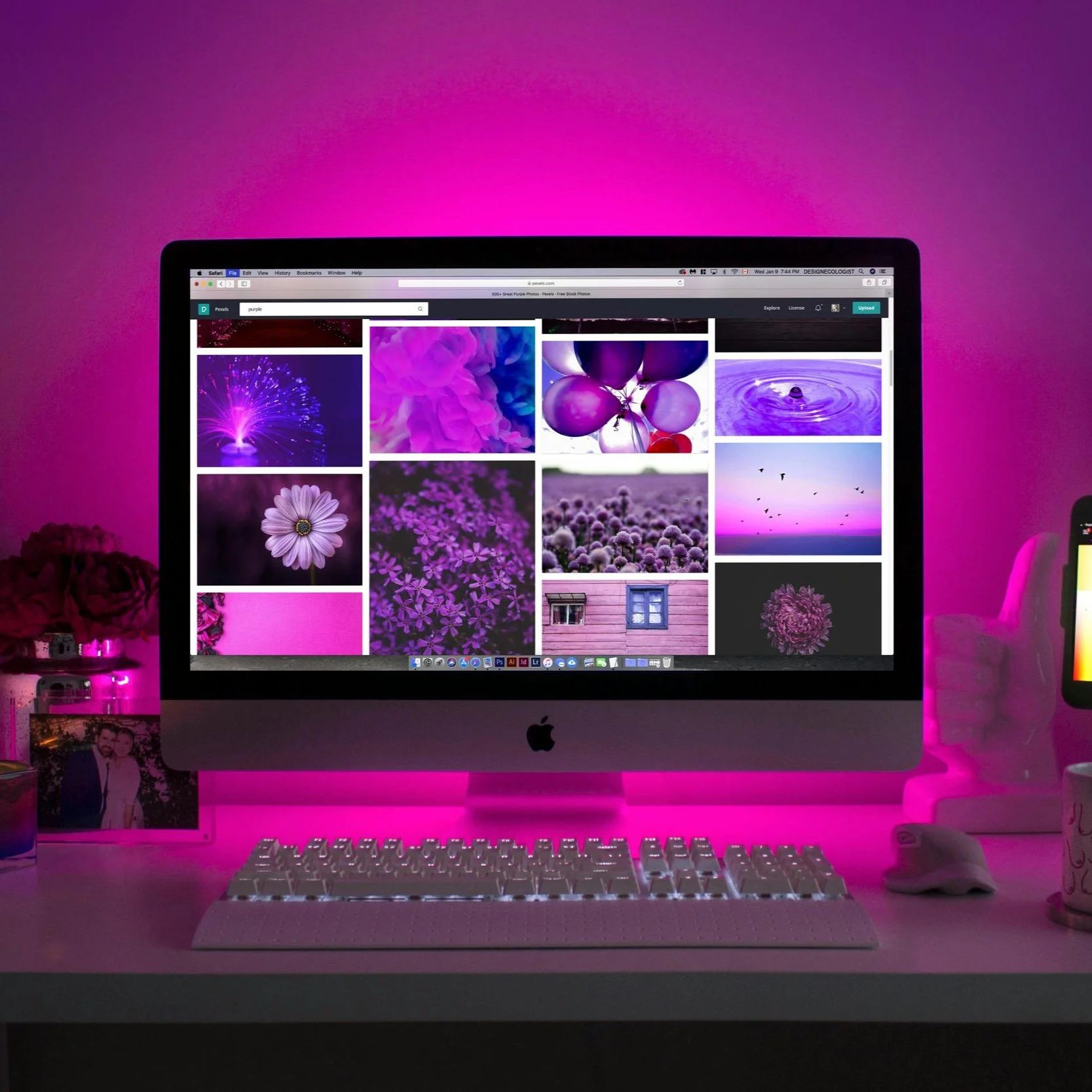 An iMac computer displaying purple-themed images on a desktop, with pink ambient LED lighting illuminating the workspace.