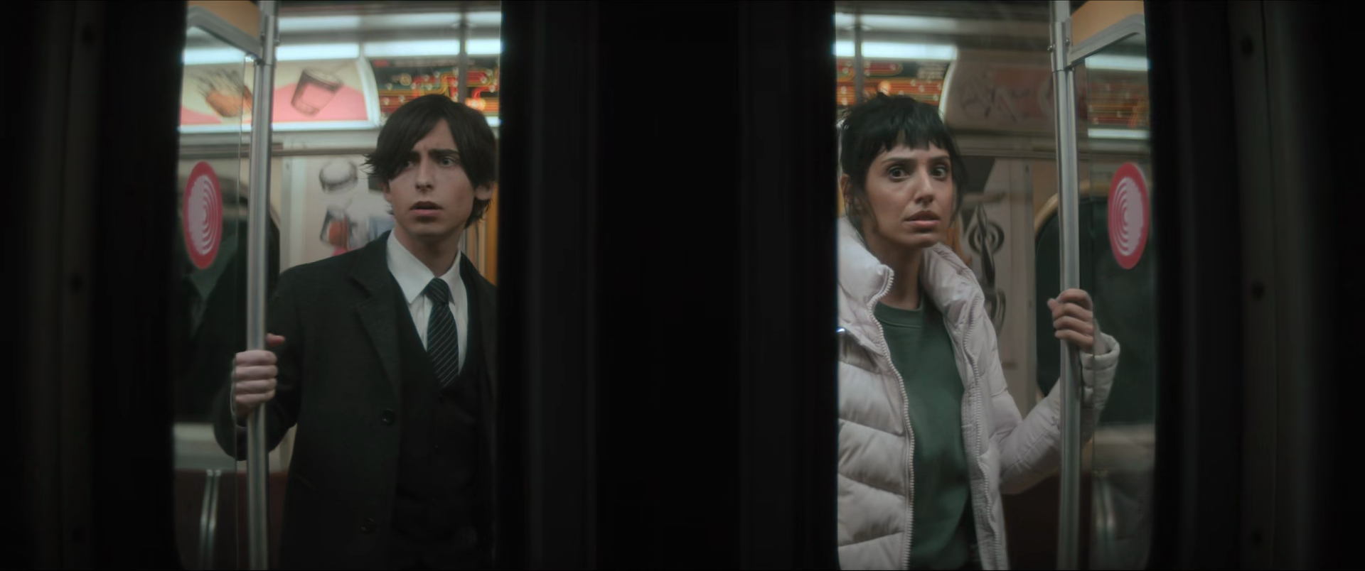 Two people, a man and a woman, standing inside a limited space near the doors of a vending machine or arcade game, looking surprised or confused.