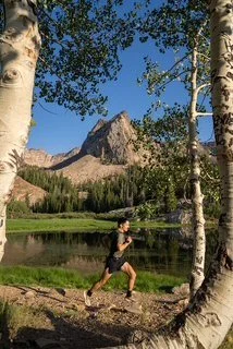 Person running along a lakeshore with mountains and trees in the background.