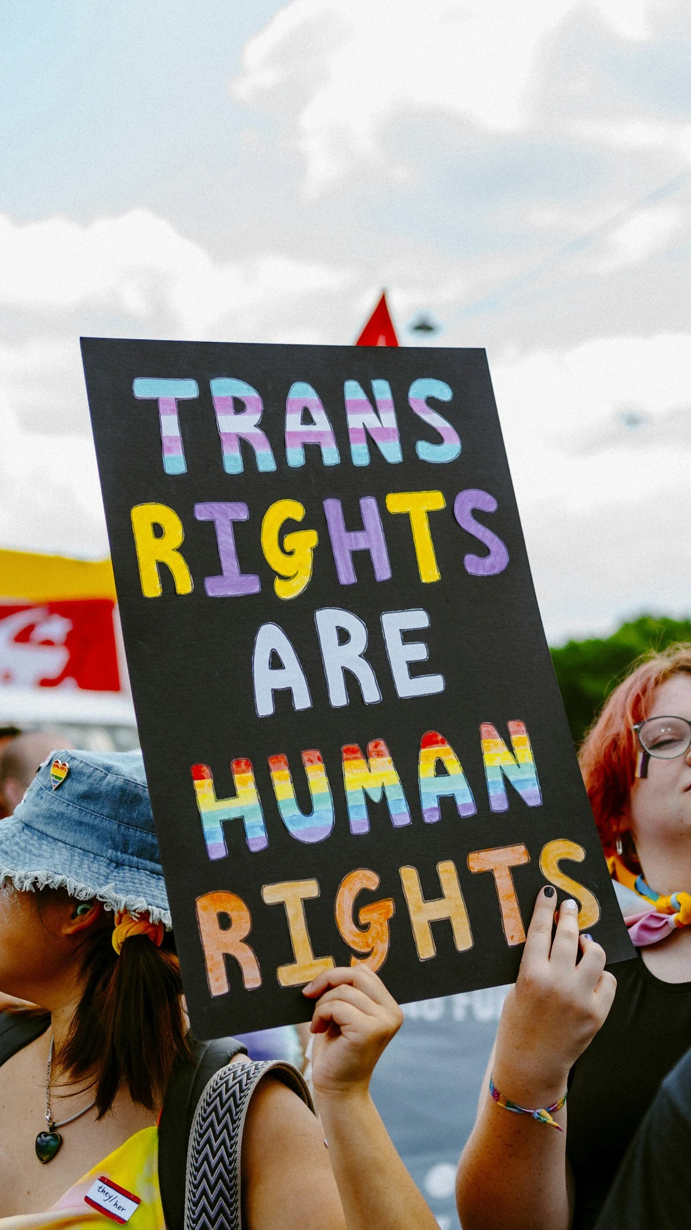 A rectangular sign with a black background and colorful words that says Trans Rights are Human Rights