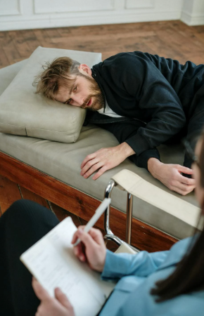 This image shows a man in a black jacket lying down and speaking with a therapist.