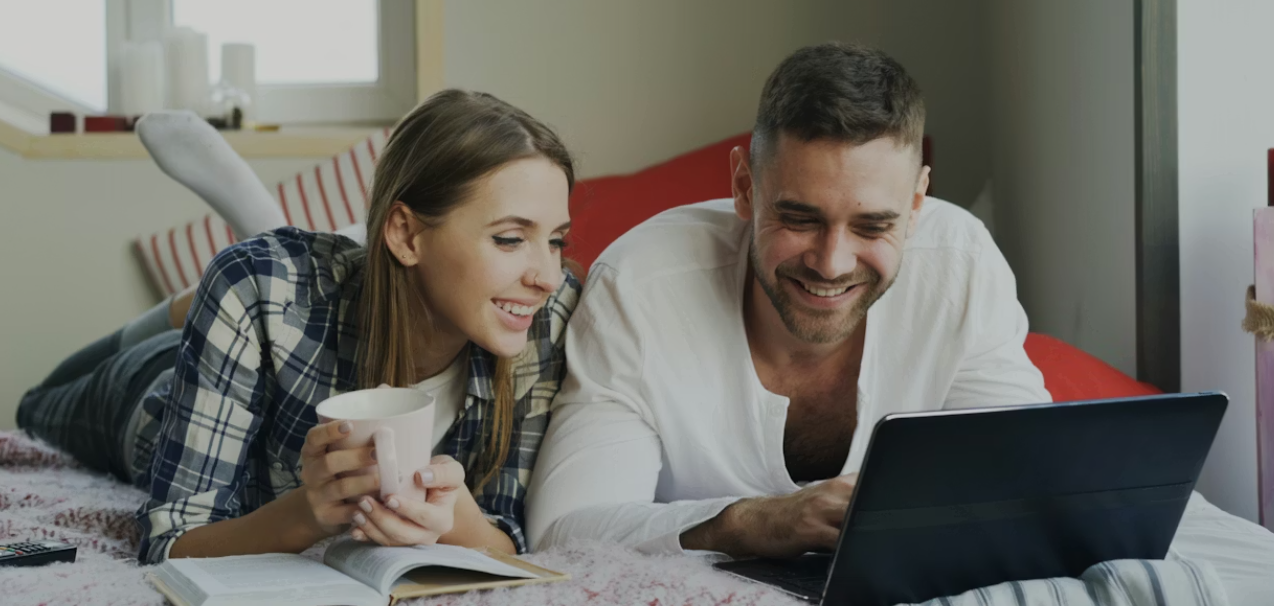 This image shows a couple lying on bed with laptop.