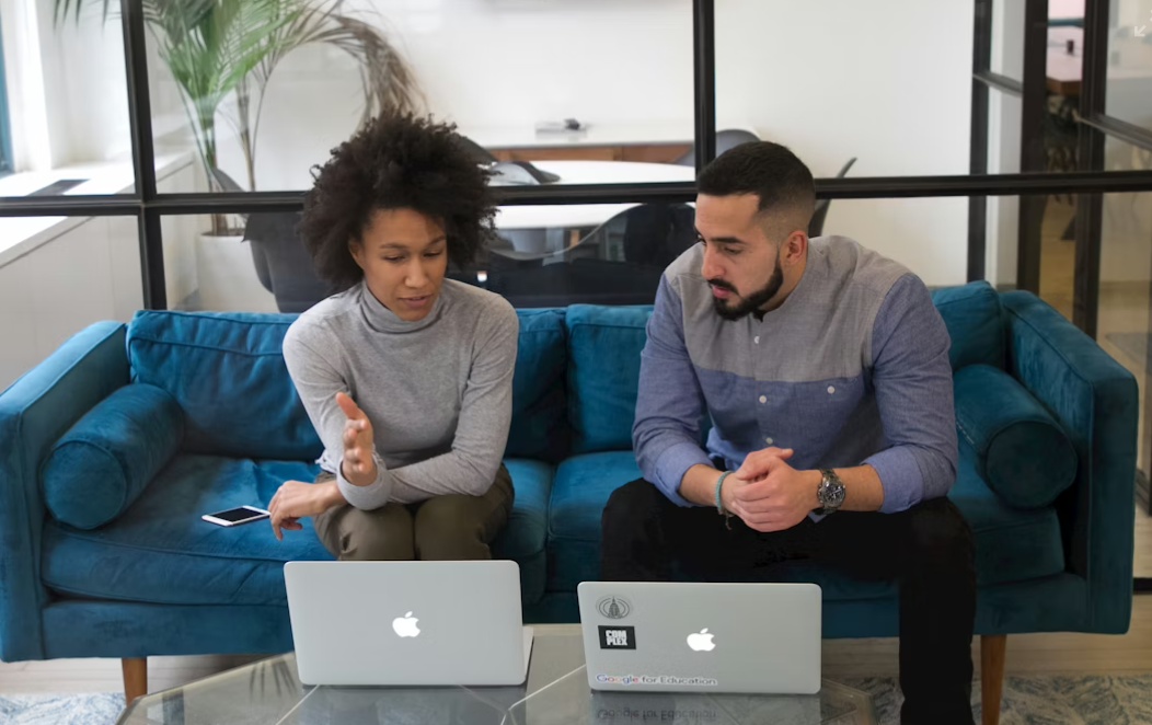 This image shows a couple sitting on a couch with their laptops.