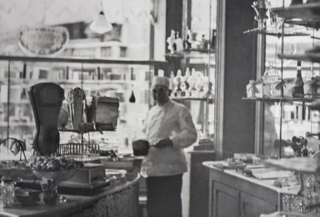 Pâtissier dans la boutique Maison Nihoul d’époque, vue en noir et blanc.”