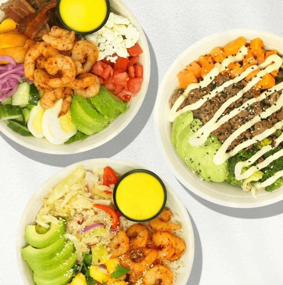 Three bowls of salads with various fresh ingredients and two small containers of yellow dressing.