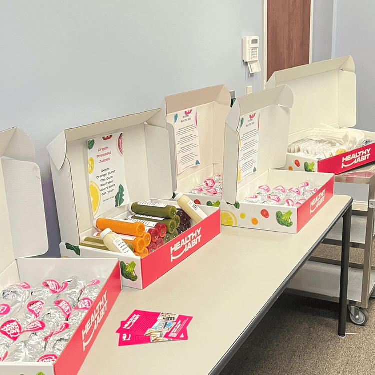 Boxes of bottled juice and water bottles on a table in a room, with promotional flyers and a wall phone in the background.