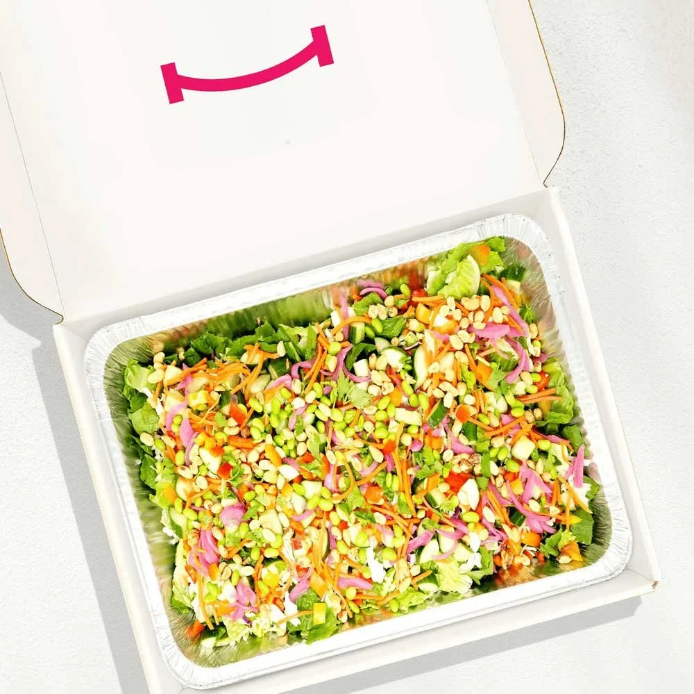 Colorful salad in a takeout container with shredded carrots, purple cabbage, lettuce, pine nuts, and other vegetables.