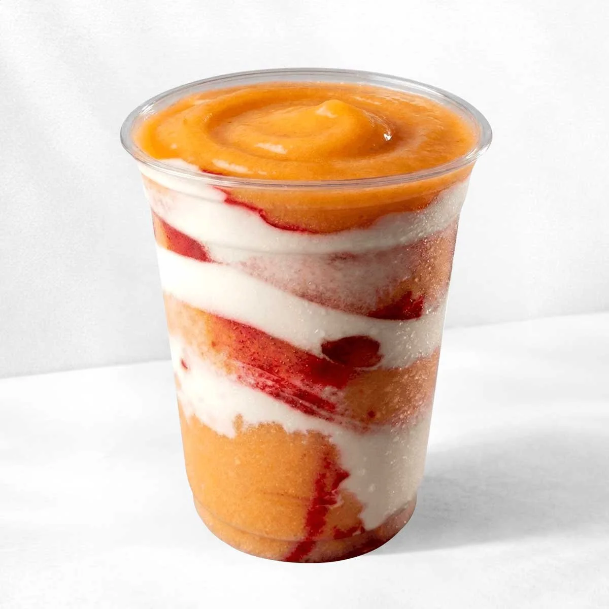 A clear plastic cup filled with layered fruit and cream, topped with a peach slice.