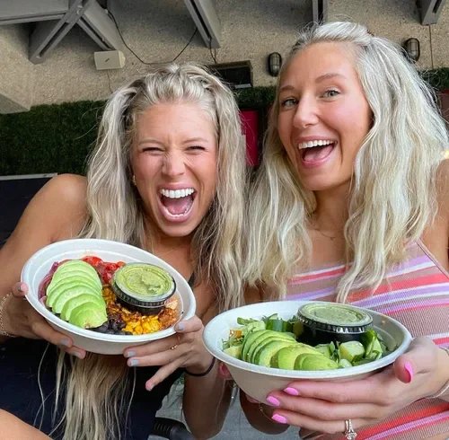 Two women with long blonde hair smiling and holding bowls of food with avocados and green sauces