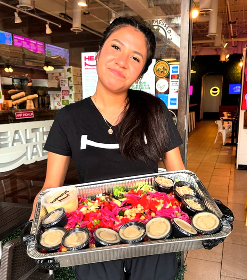 A woman holding a tray of food with colorful flowers and small containers of sauce inside a restaurant