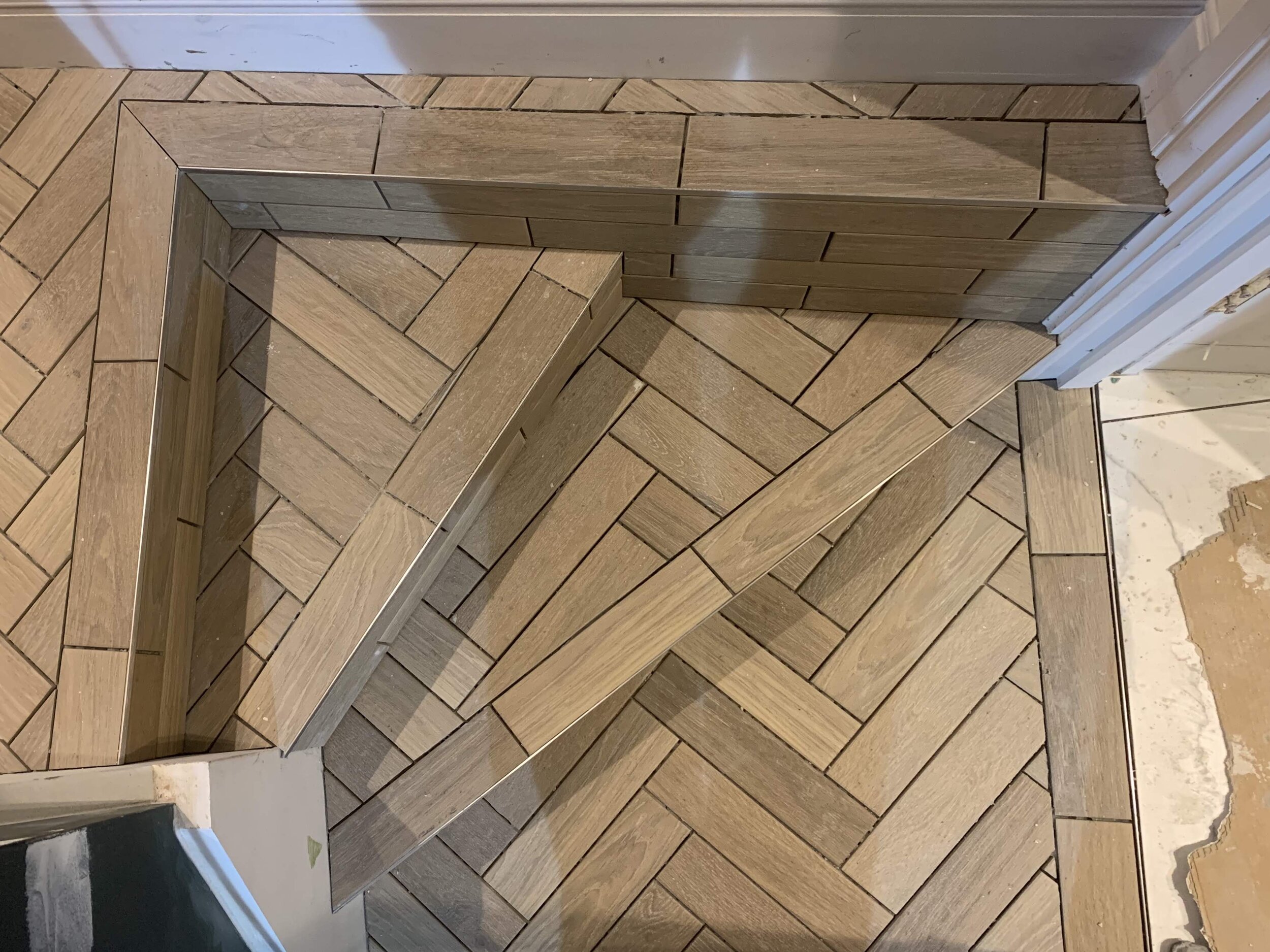 Wood effect tiles used in a Herringbone pattern flowing down two steps in a hallway.