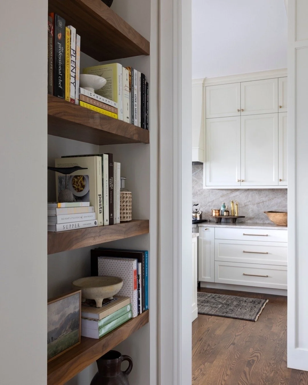 A tucked-away bookshelf adds warmth and soul to this transition space. Natural walnut shelves, filled with well-loved cookbooks and collected pottery, balance beautifully against crisp cabinetry and soft stone textures.
We love designing these in-be