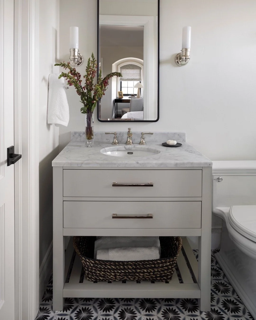This cozy bathroom proves that style doesn’t require extra square footage. We paired a soft gray vanity with a marble countertop for timeless sophistication, then added warmth through texture, like the woven basket and fresh greenery. The state