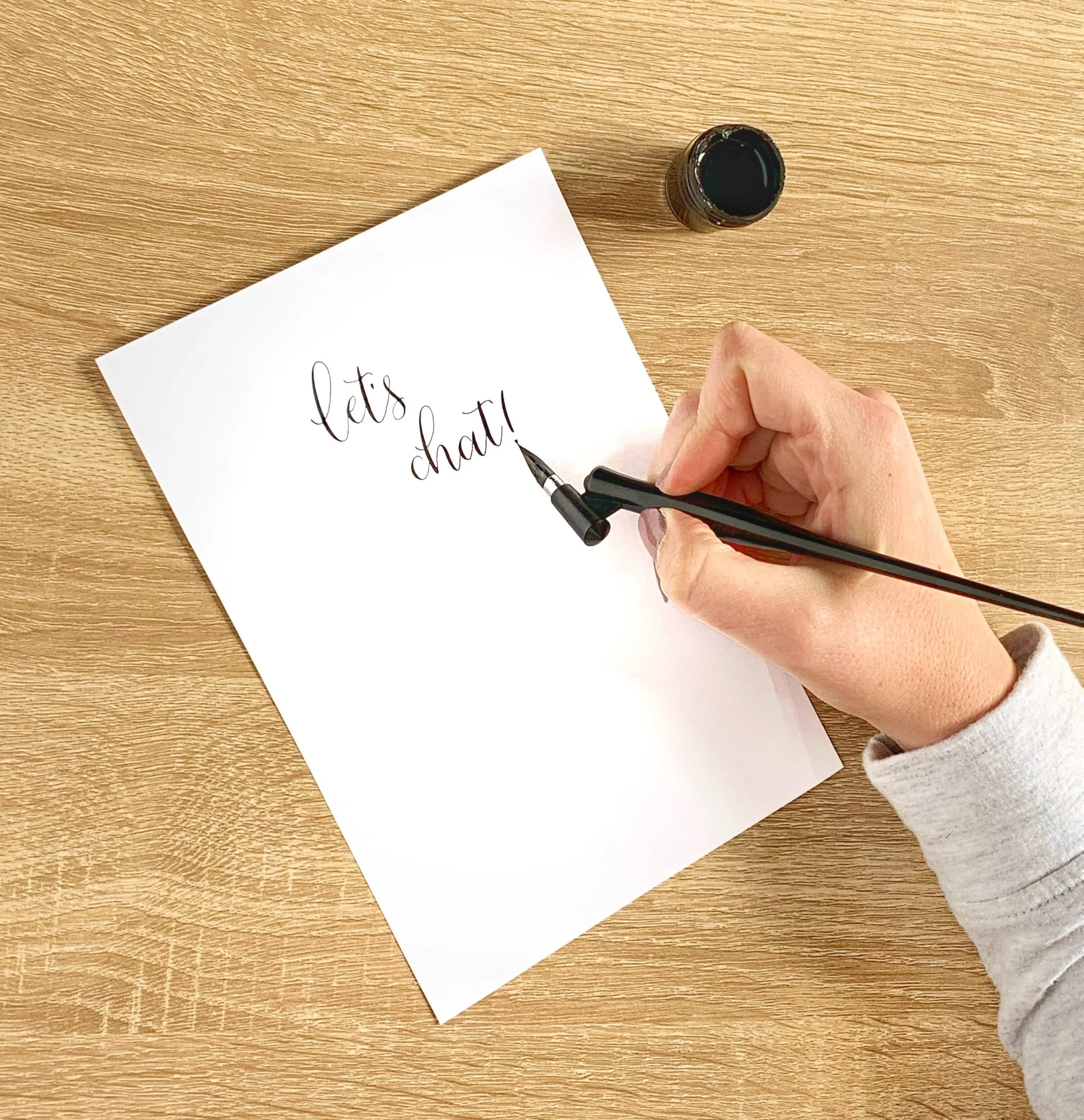 paper and hand holding a calligraphy pen on a desk with calligraphy writing