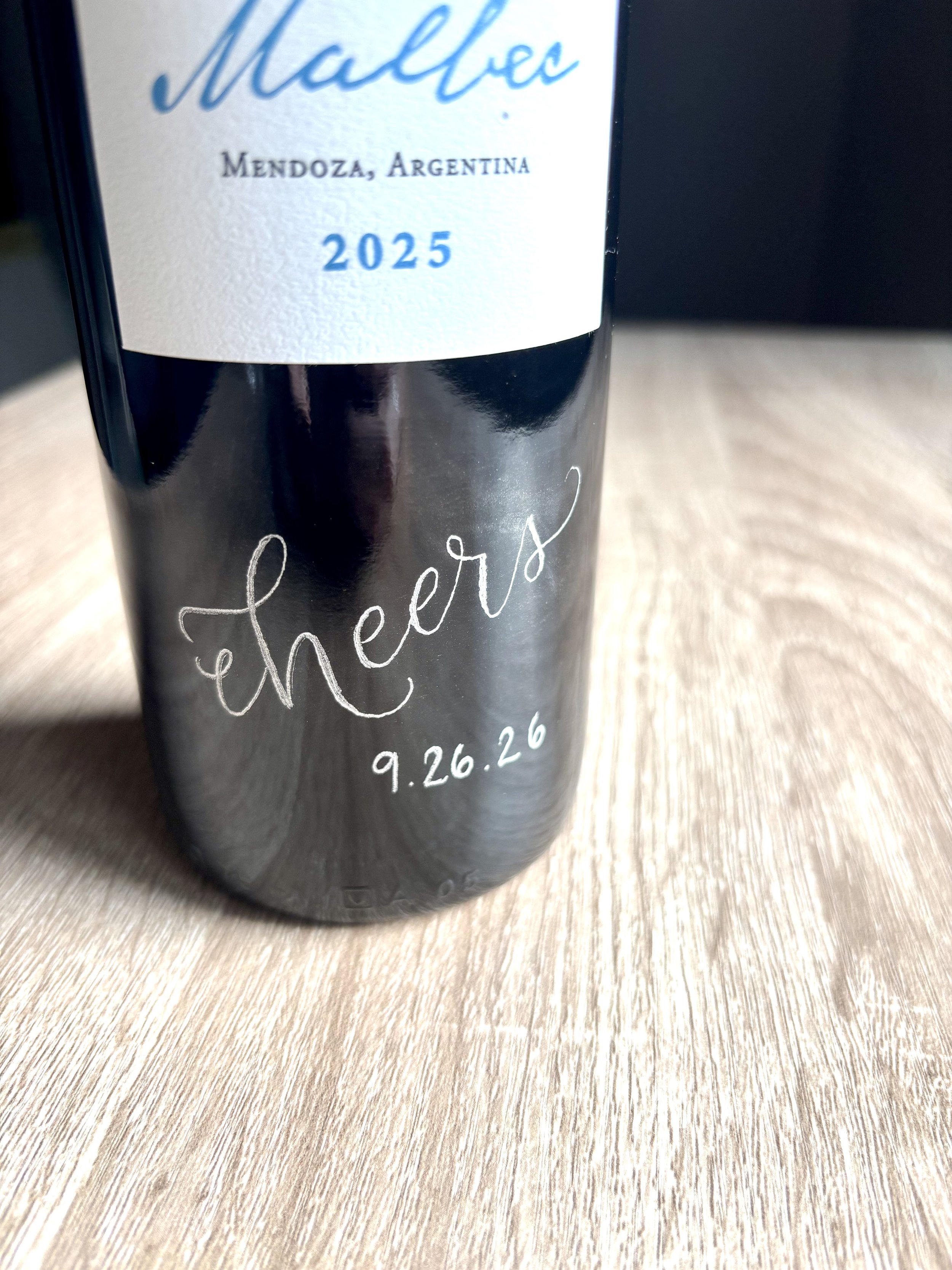 wine bottle with hand engraved calligraphy spelling cheers with a wedding date