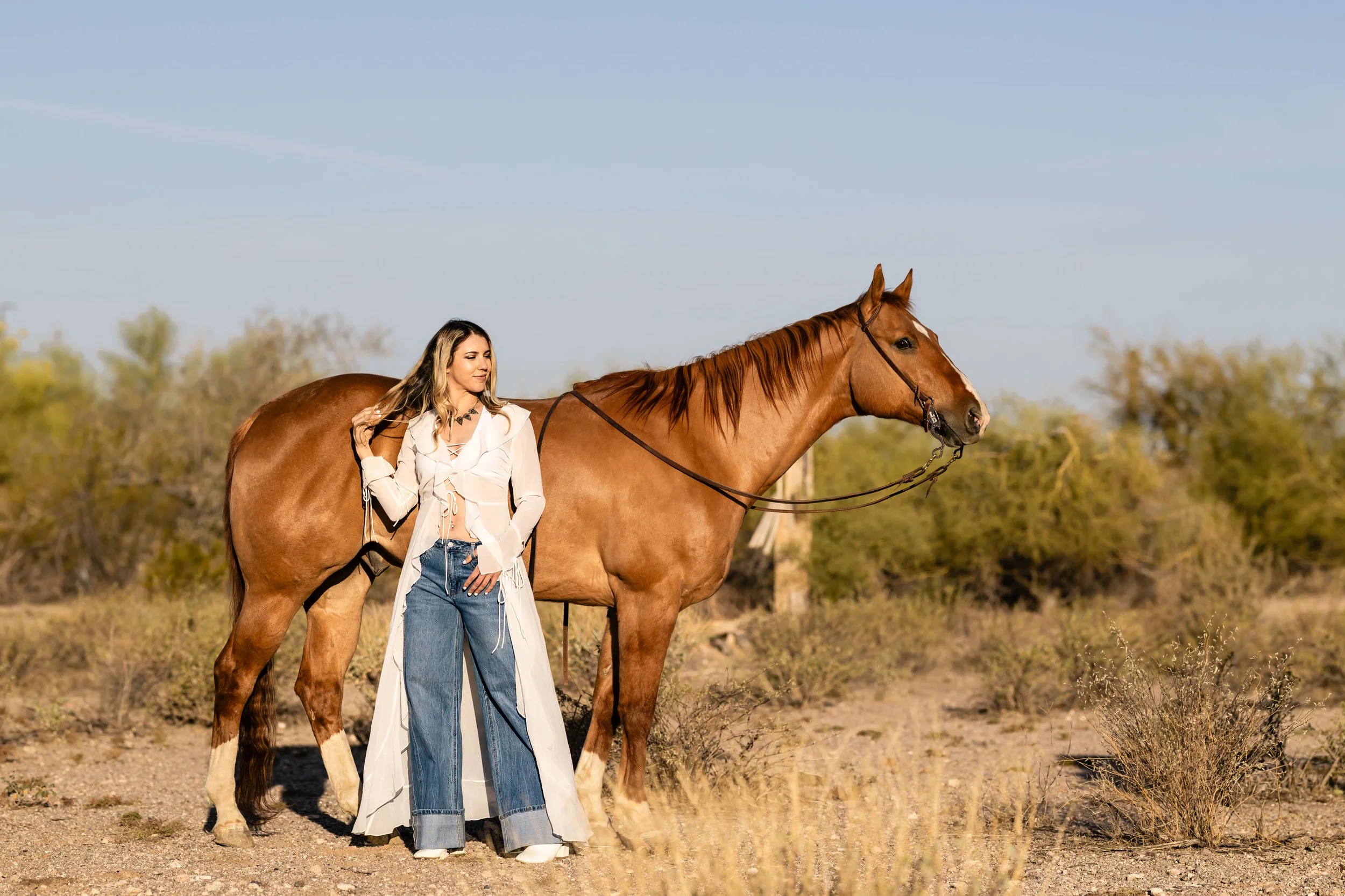 A woman standing next to a chestnut horse in a desert landscape during daytime.