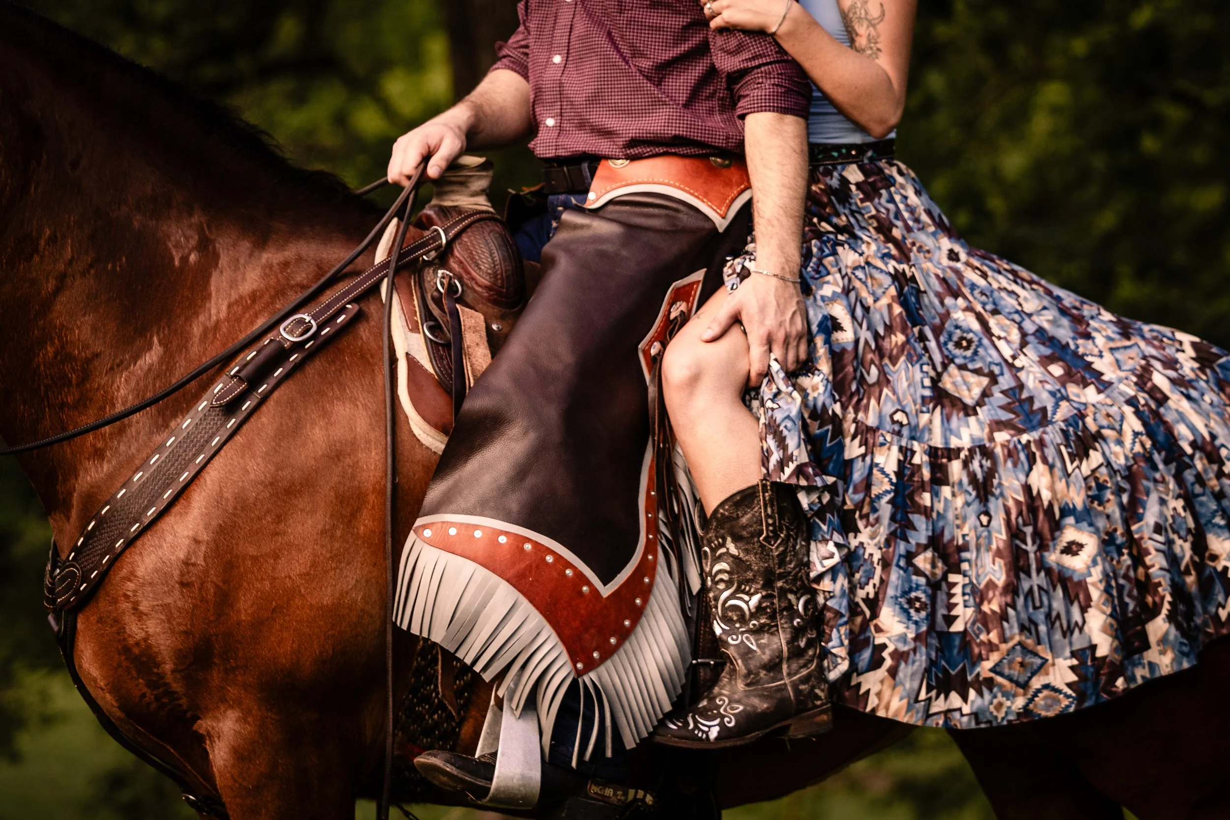 Close-up of a person riding a horse, wearing cowboy boots, a patterned skirt, and western attire.