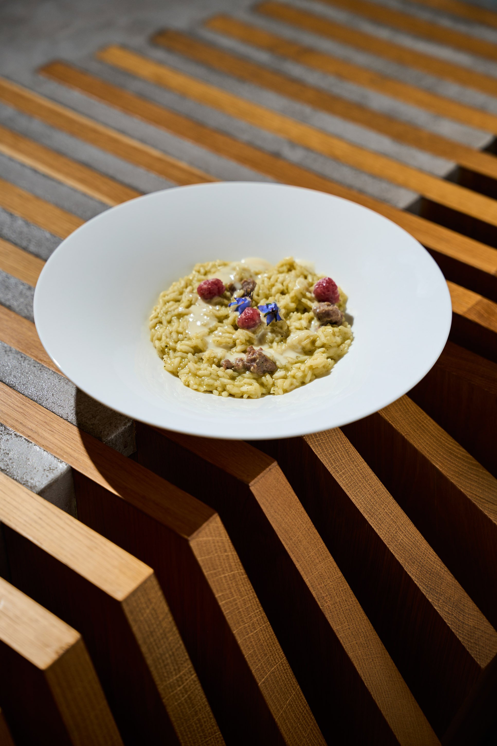 Fotografia food professionale di risotto cremoso con lamponi e fiori di borragine su struttura in legno, ristorante gourmet a Milano — Cardinali Studio