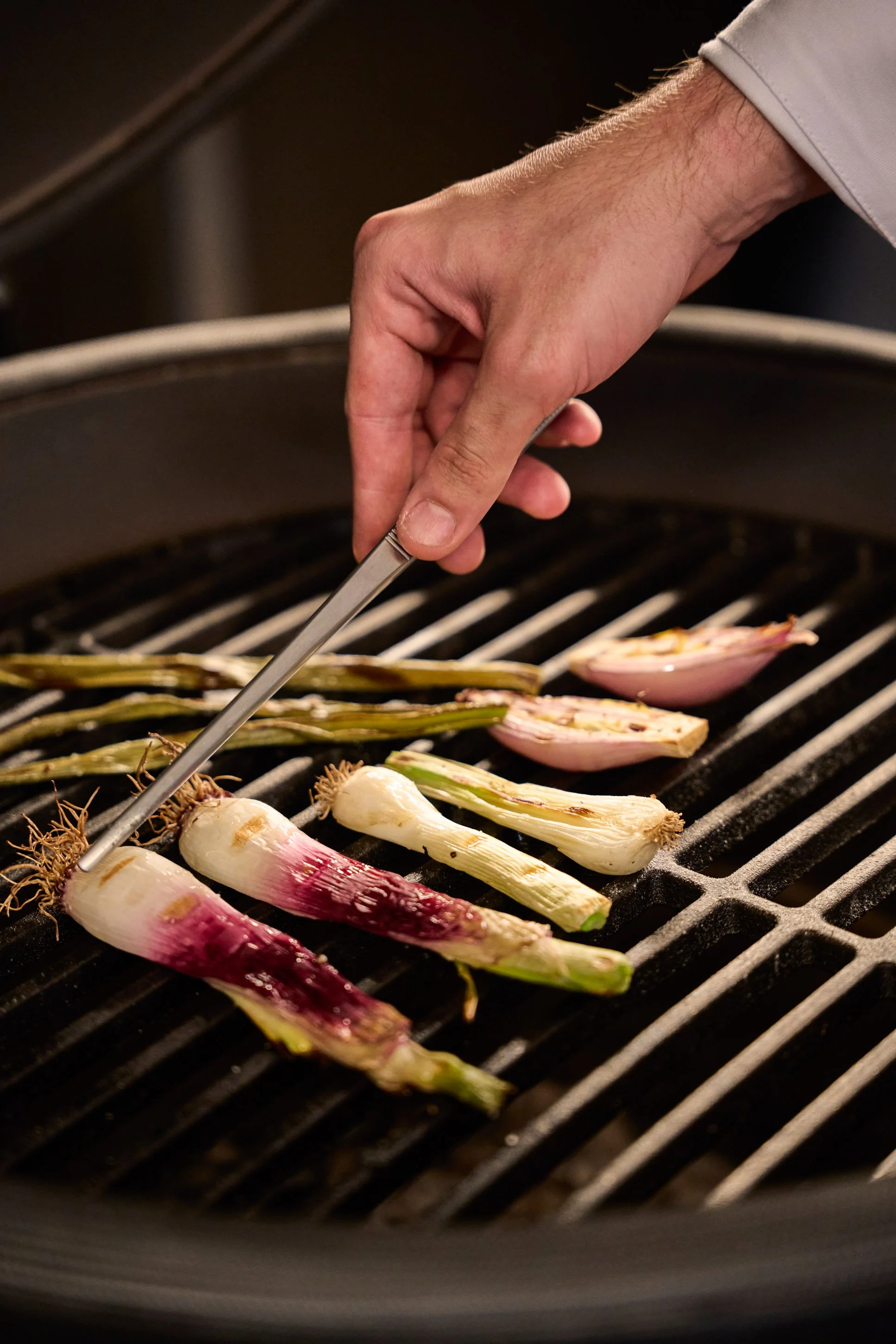Fotografia food professionale: chef griglia cipolle e scalogni su griglia rotonda in cucina di ristorante a Milano — Cardinali Studio