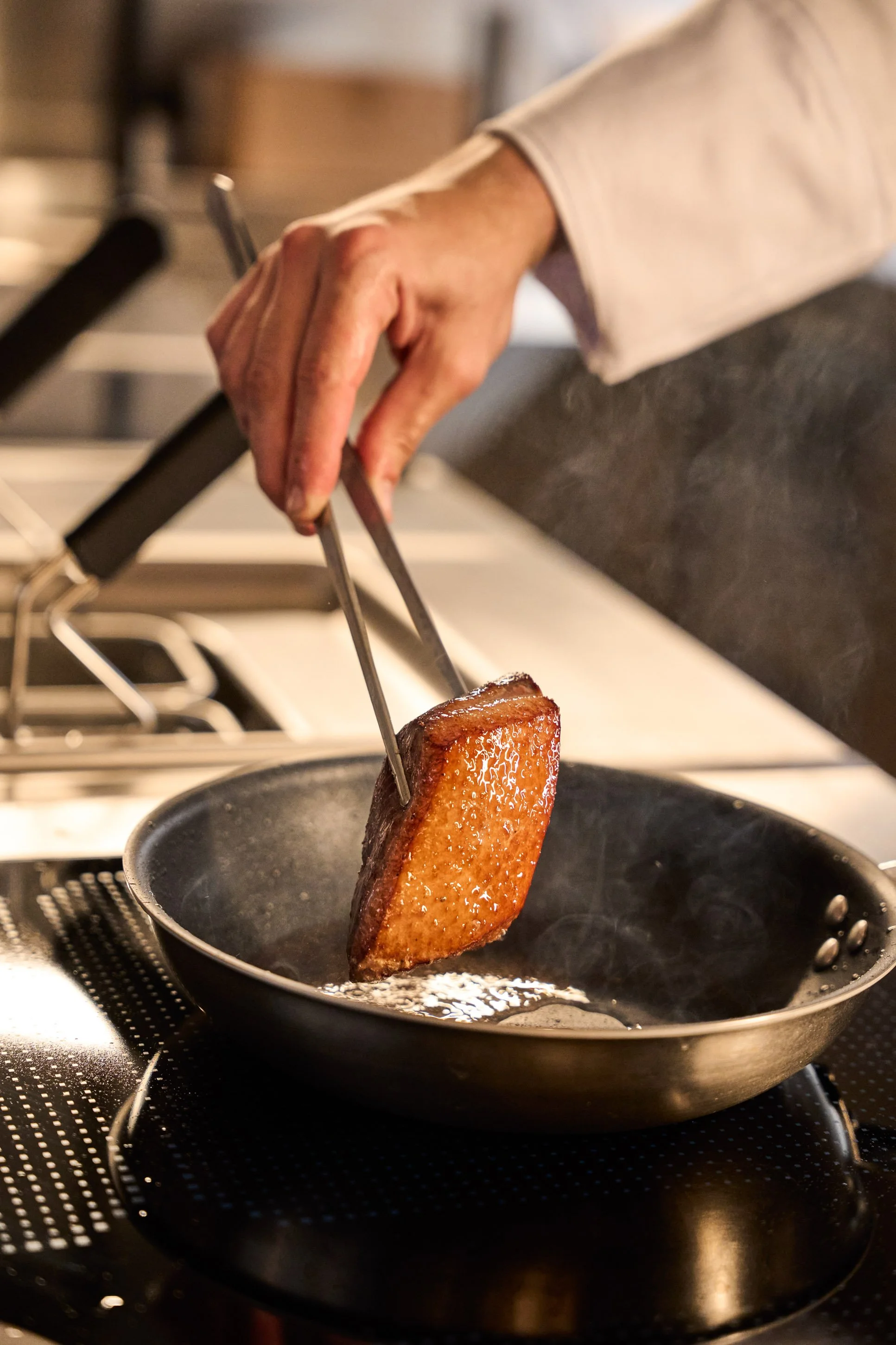 Fotografia food professionale: chef gira petto d'anatra in padella durante la cottura in cucina di ristorante a Milano — Cardinali Studio