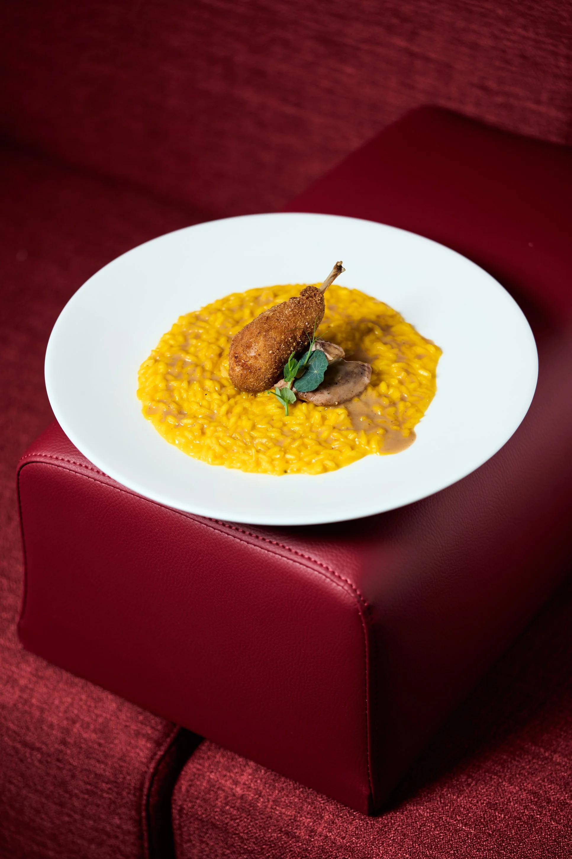 Fotografia food professionale di risotto allo zafferano con quaglia e funghi su sfondo bordeaux, ristorante gourmet a Milano — Cardinali Studio