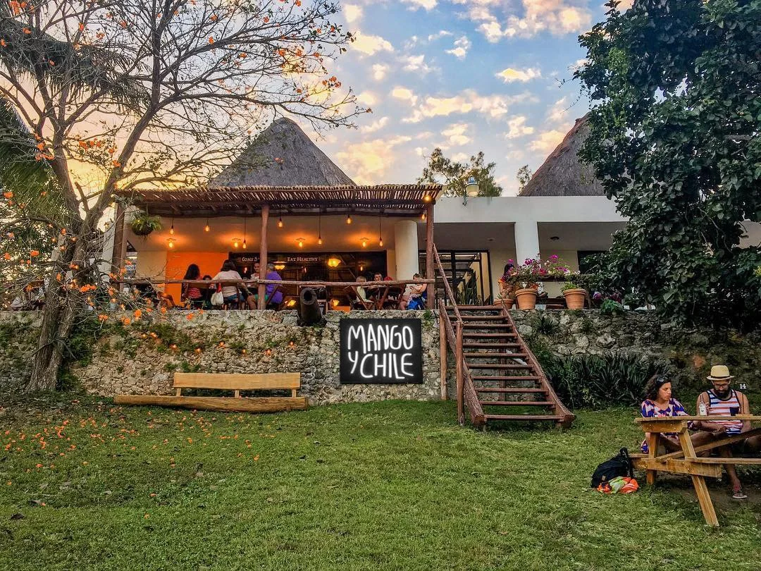 Restaurant Mango y Chile at the top of the hill with a privileged view of Bacalar lagoon, with people dining and socializing. 