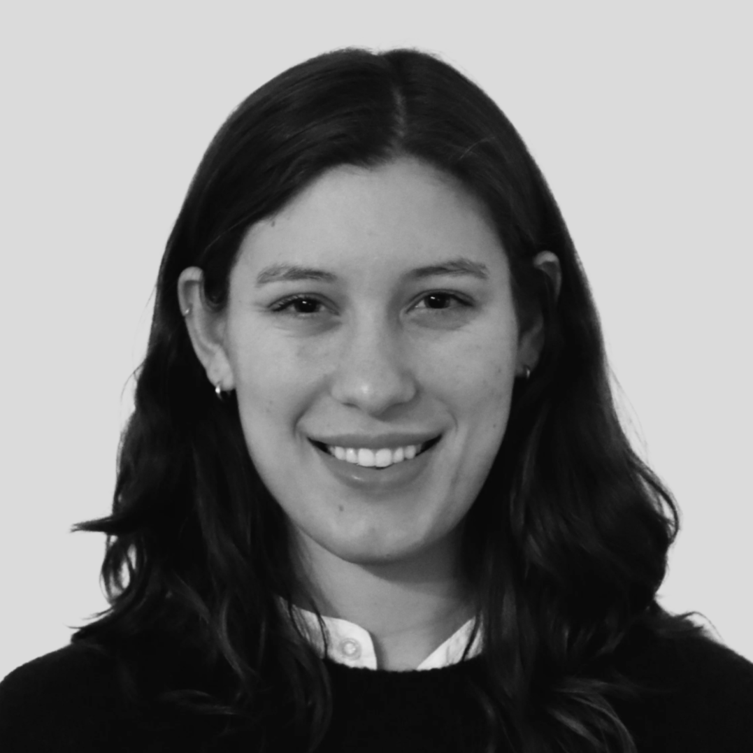 Black and white portrait of a smiling woman with shoulder-length wavy hair, wearing earrings, a white collared shirt, and a dark sweater.