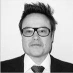 A black-and-white photo of a man with dark hair, glasses, wearing a suit and tie.