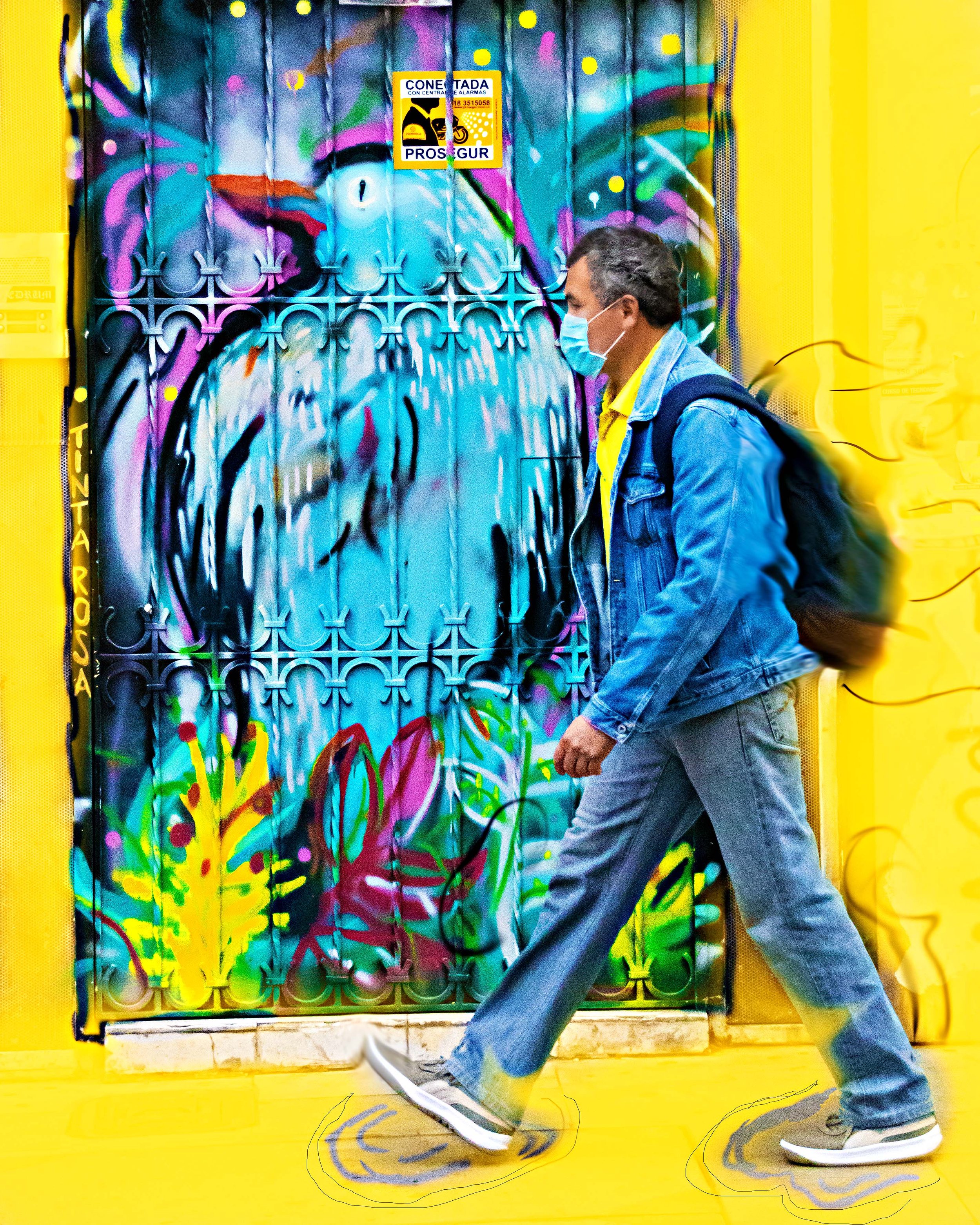 A man walking by a graffiti bird on the street.