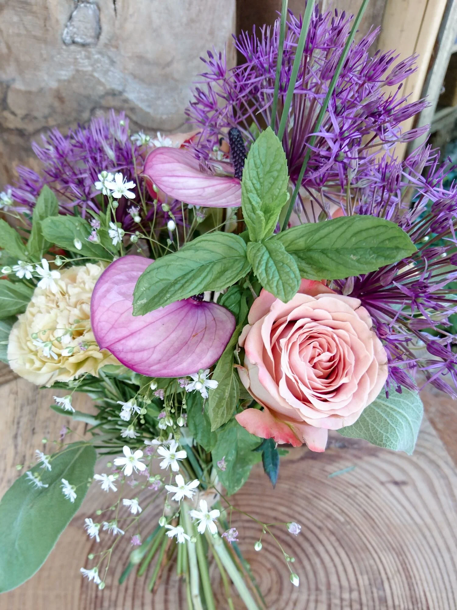 Spring bouquet of alium purple flowers, cappuccino roses, anthurium and wild mint
