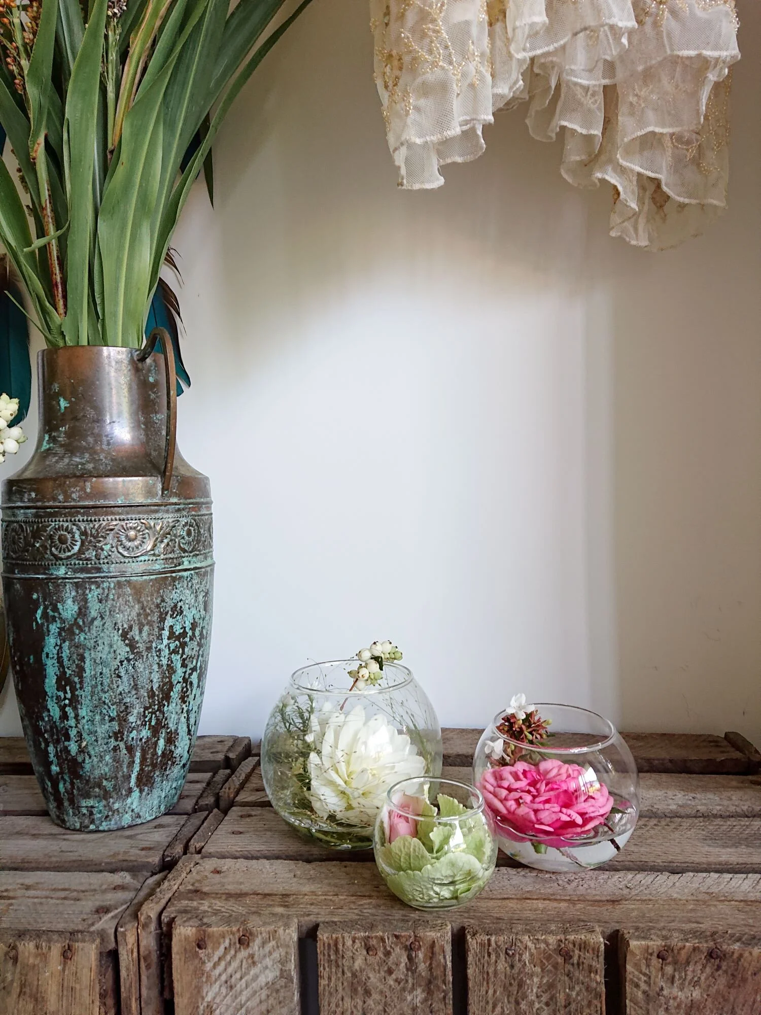 Vintage 1930's copper and turquoise rusted vase next to three small glass bowls filled with pink, white and green flowers.