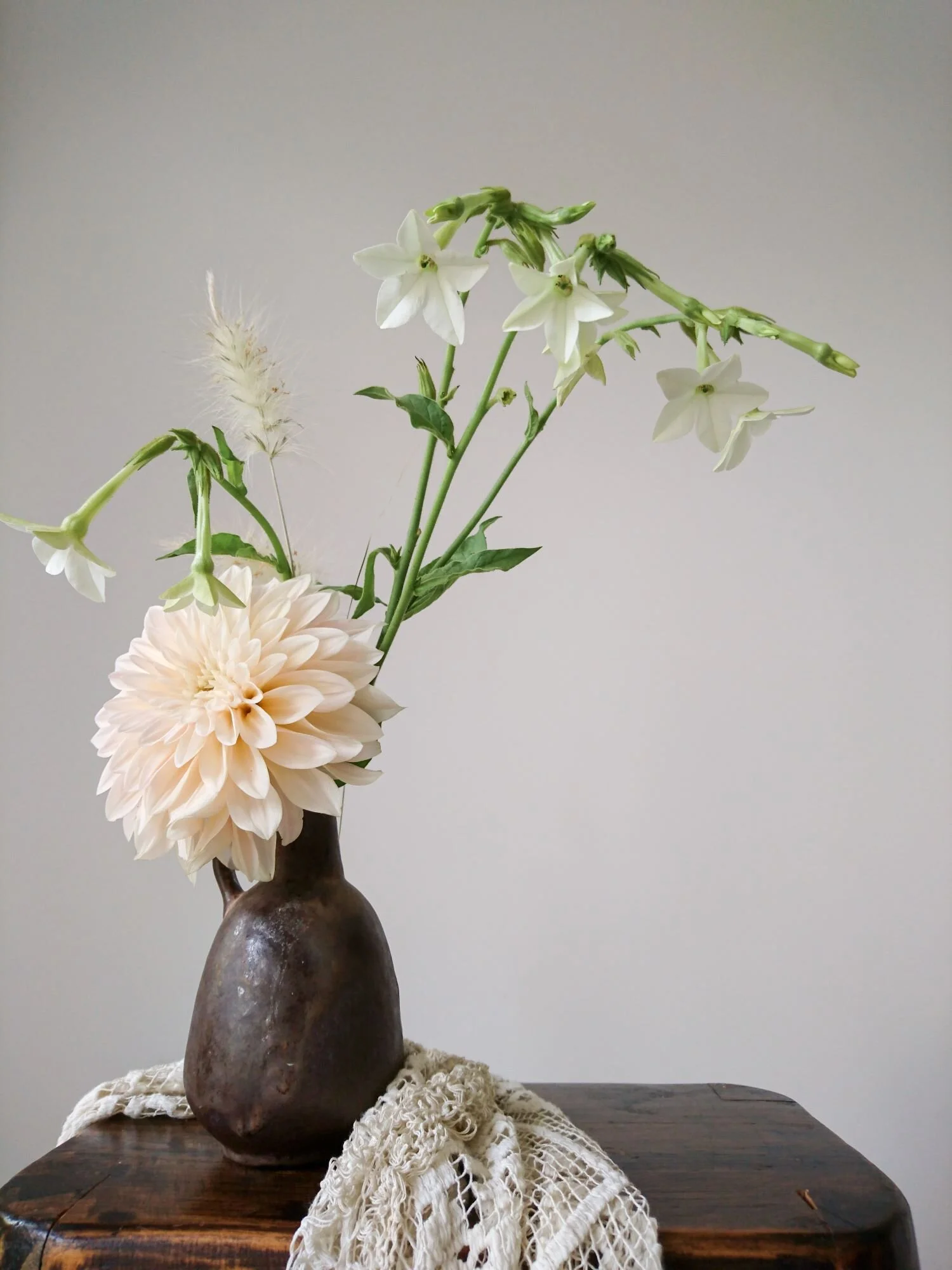 Pale cream dahlia and white tobacco flowers in a small dark brown pottery vase. 
