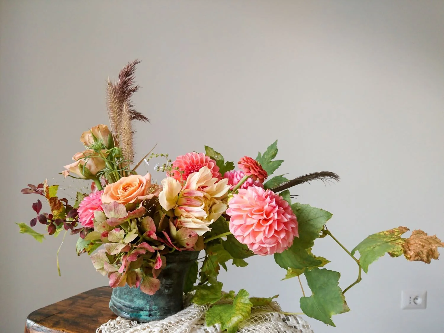 Turquoise copper vase with a mix of autumn leaves and peach coloured flowers. 