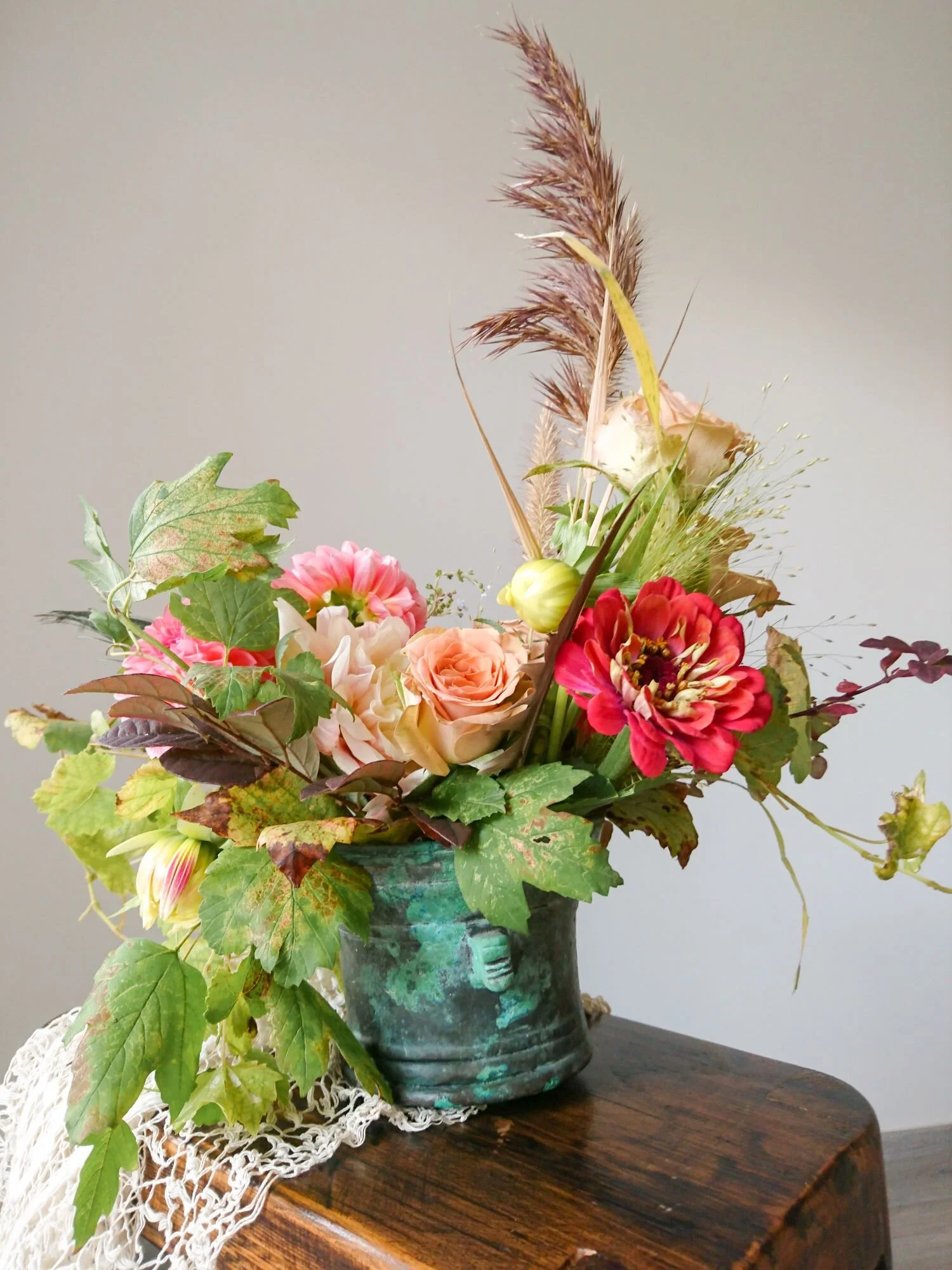 Turquoise copper vase with a mix of autumn leaves and peach coloured flowers. 