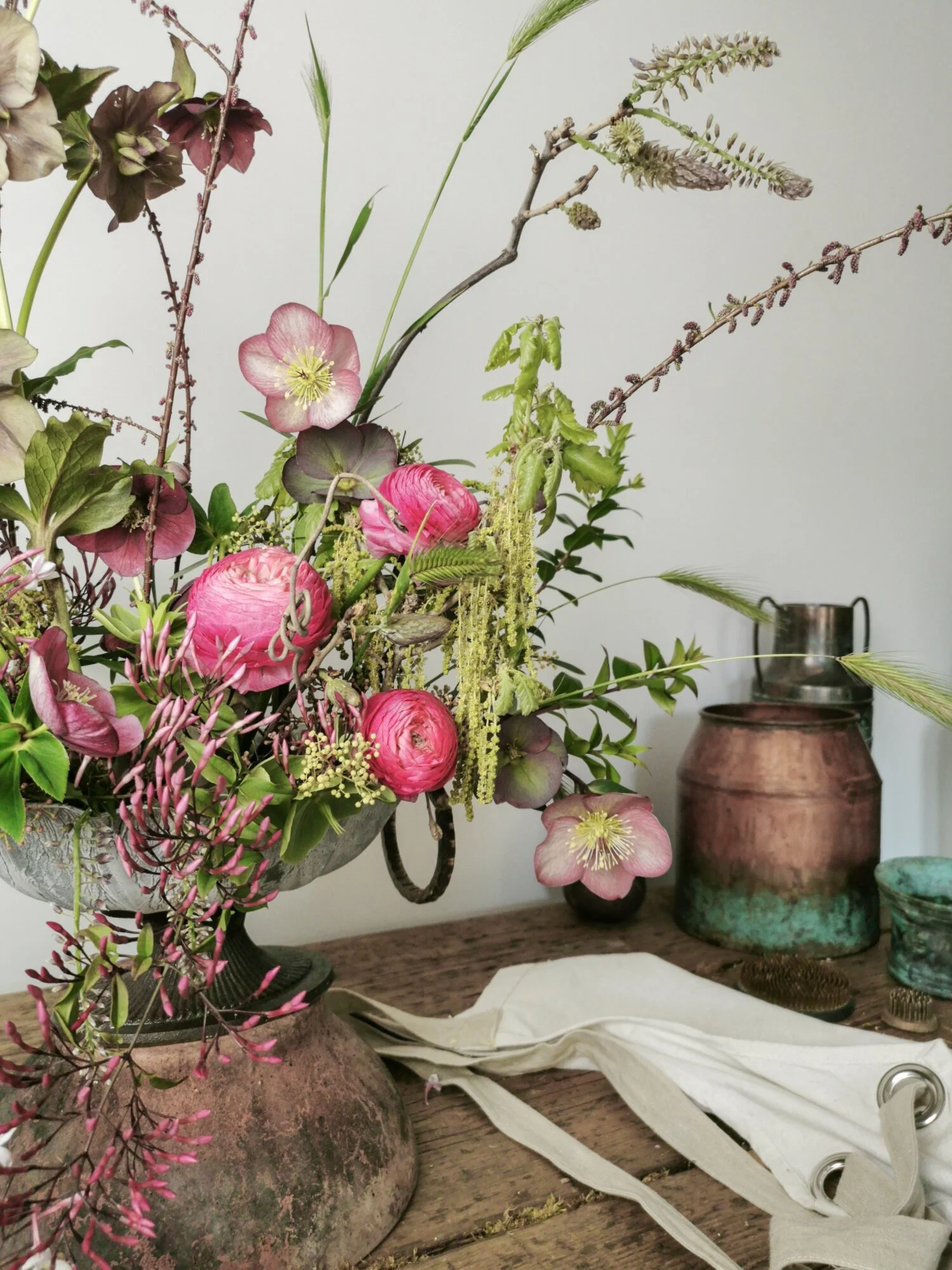 Urn arrangement of spring flowers. Pink ranunculus and hellebores and jasmine. Composizione di fiori di primavera. Ellebori rosa e gelsomino.