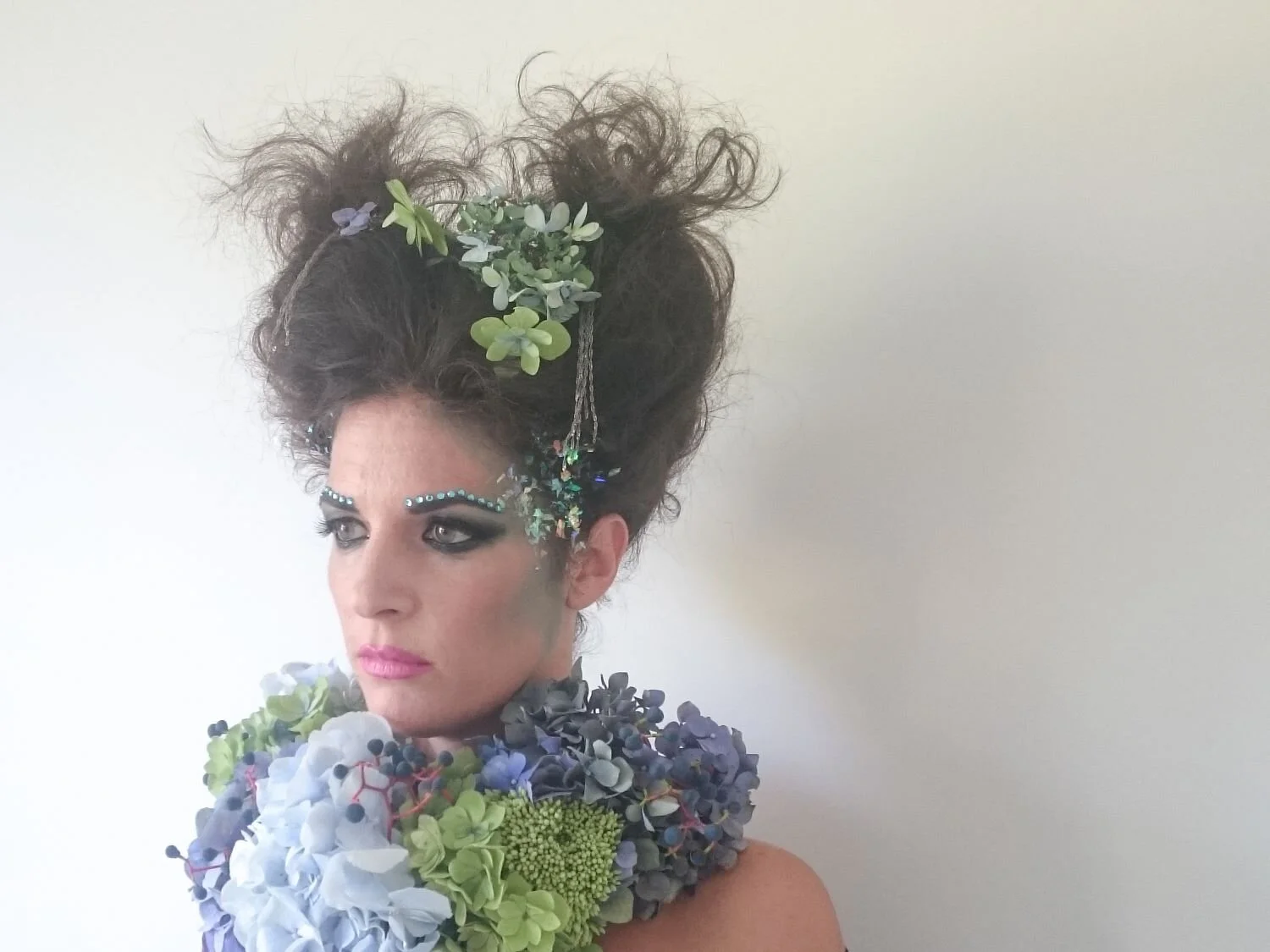 Modella con collana di ortensie blu e verdi, trucco per servizio fotografico. e fiori nei capelli