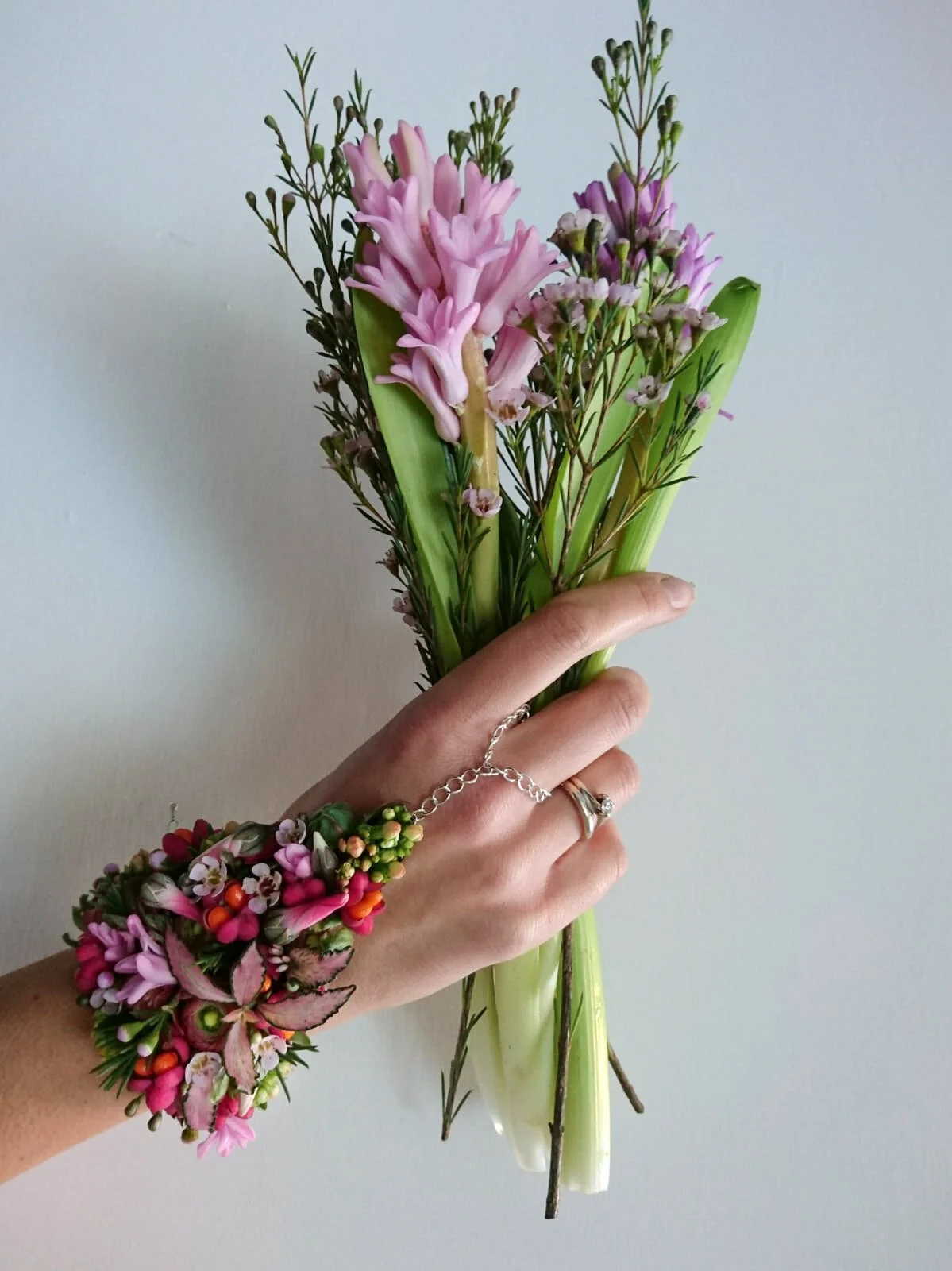Mano con braccialetto di fiori freschi, che tiene un mazzetto di giacinti. Perfetto per una sposa al matrimonio. Accessori floreali insoliti