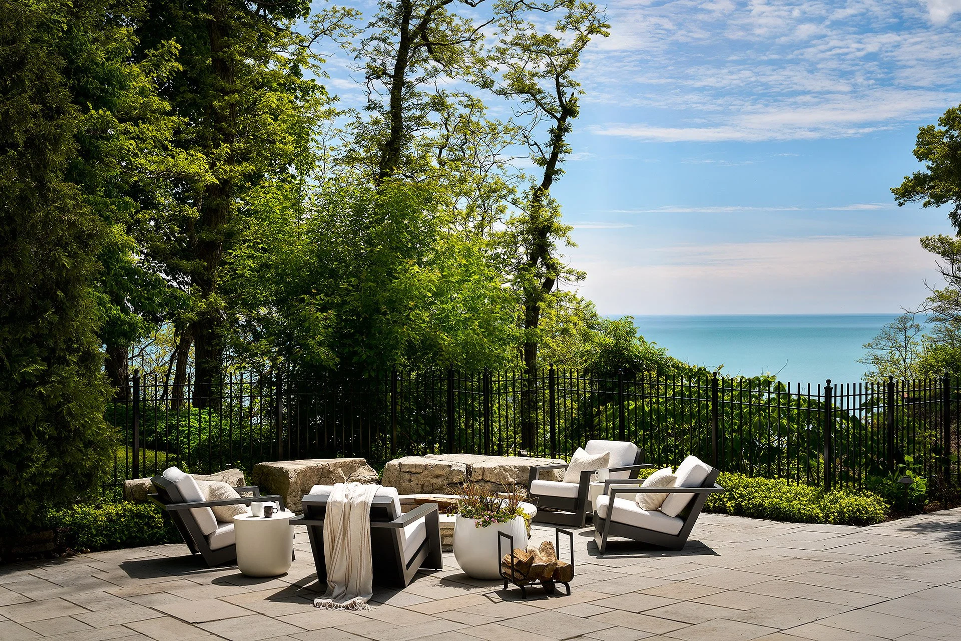 Patio area with lounge chairs and small table overlooking trees and a body of water in the background.