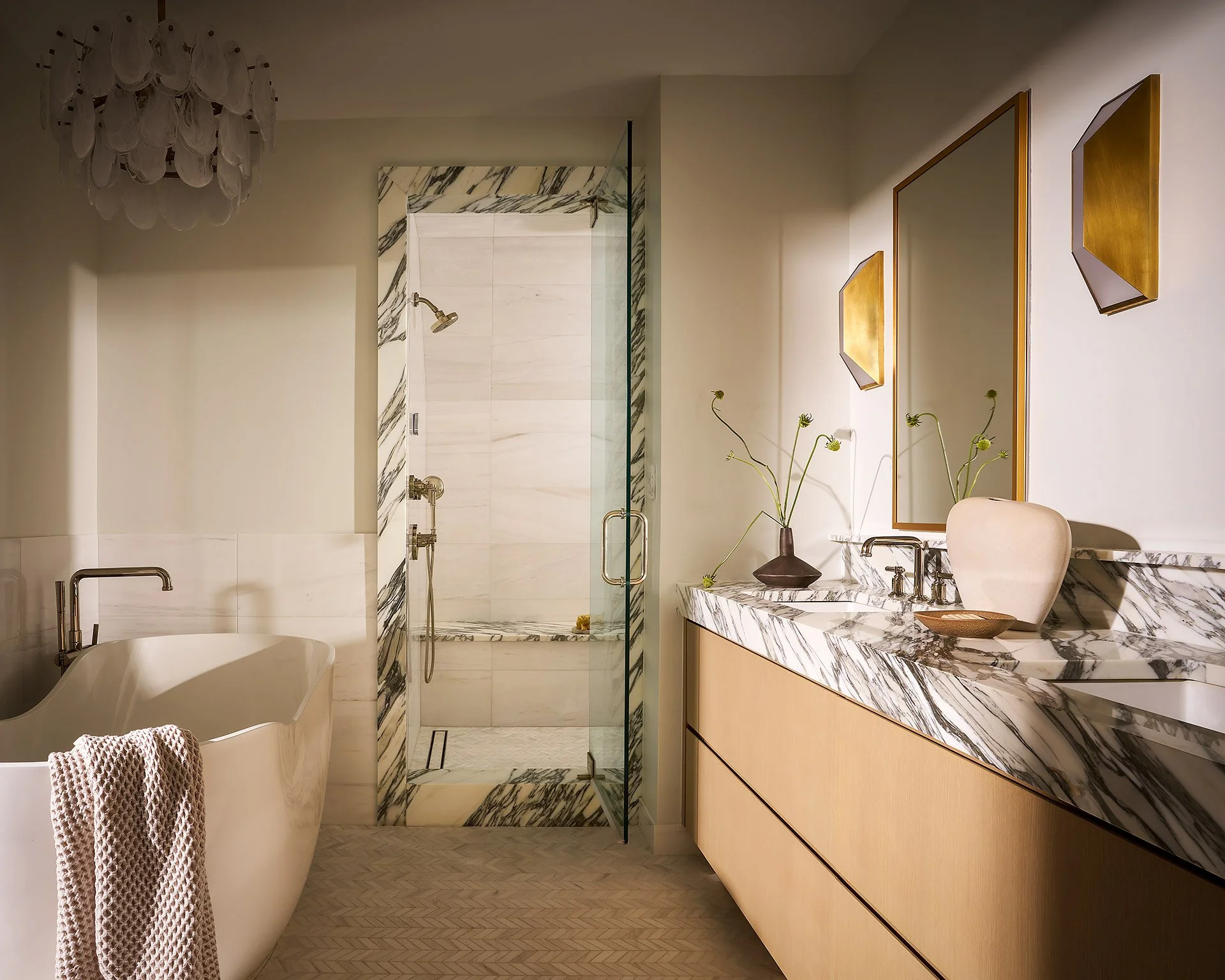 Modern bathroom with a free-standing bathtub, a marble-topped vanity, and a glass-enclosed shower with marble accents.